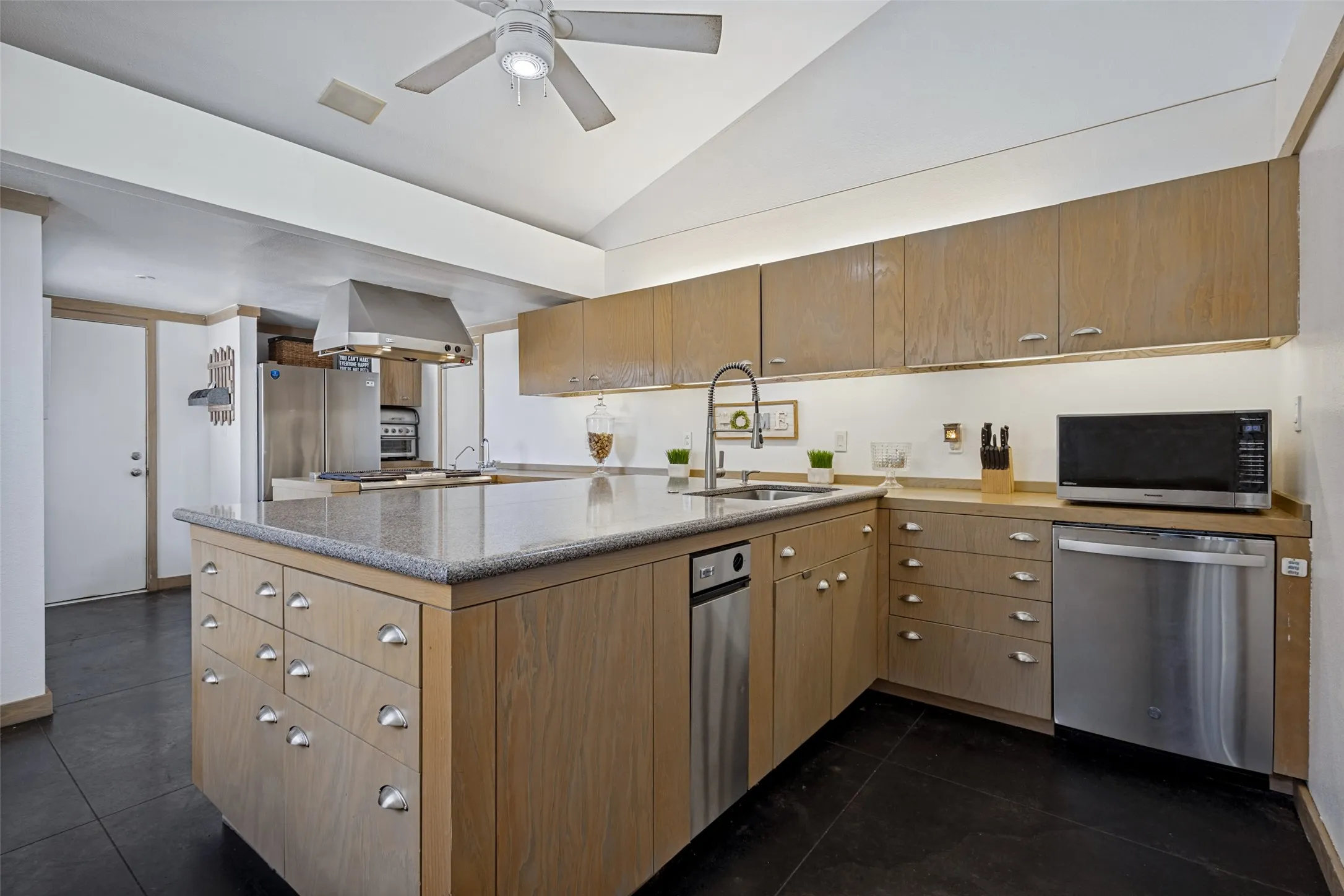 Stained concrete is on the floor and a breezy ceiling fan is above.  Under and above cabinet lighting adds to the bright cheerful appeal of the kitchen.  Natural wood trim on the walls and baseboards match the cabinetry.