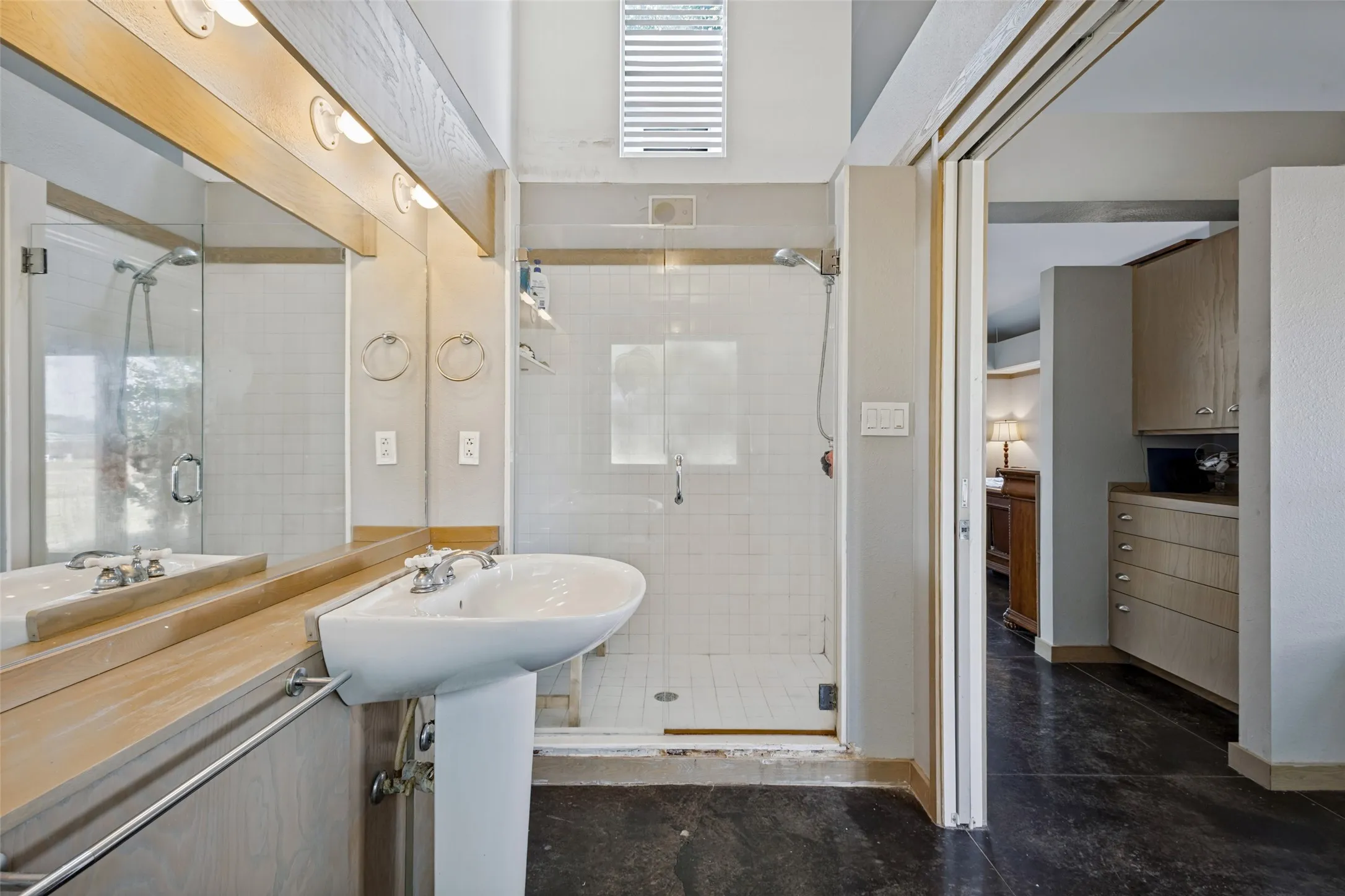 The primary bath has a roomy shower with a window above to allow light into the space.  Beyond in the area between the bath and the bedroom there is a built-in bureau.