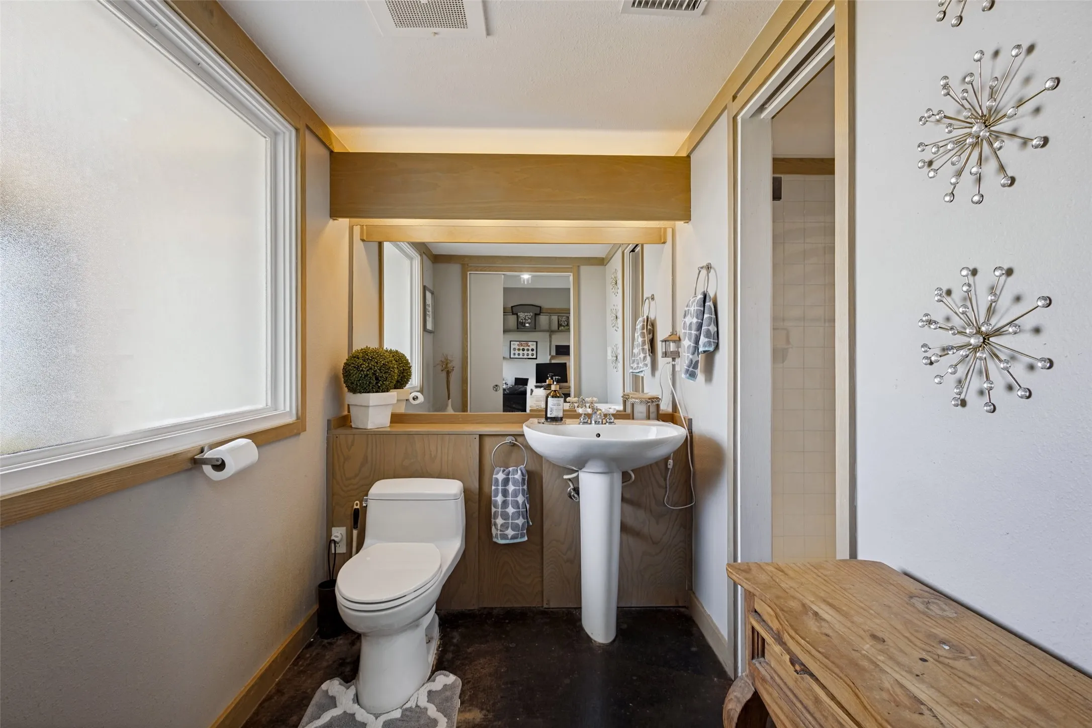 This bath is attached to the office/bedroom.  It has natural wood cabinets, a pedestal sink and a shower.  Stained concrete is on the floor.