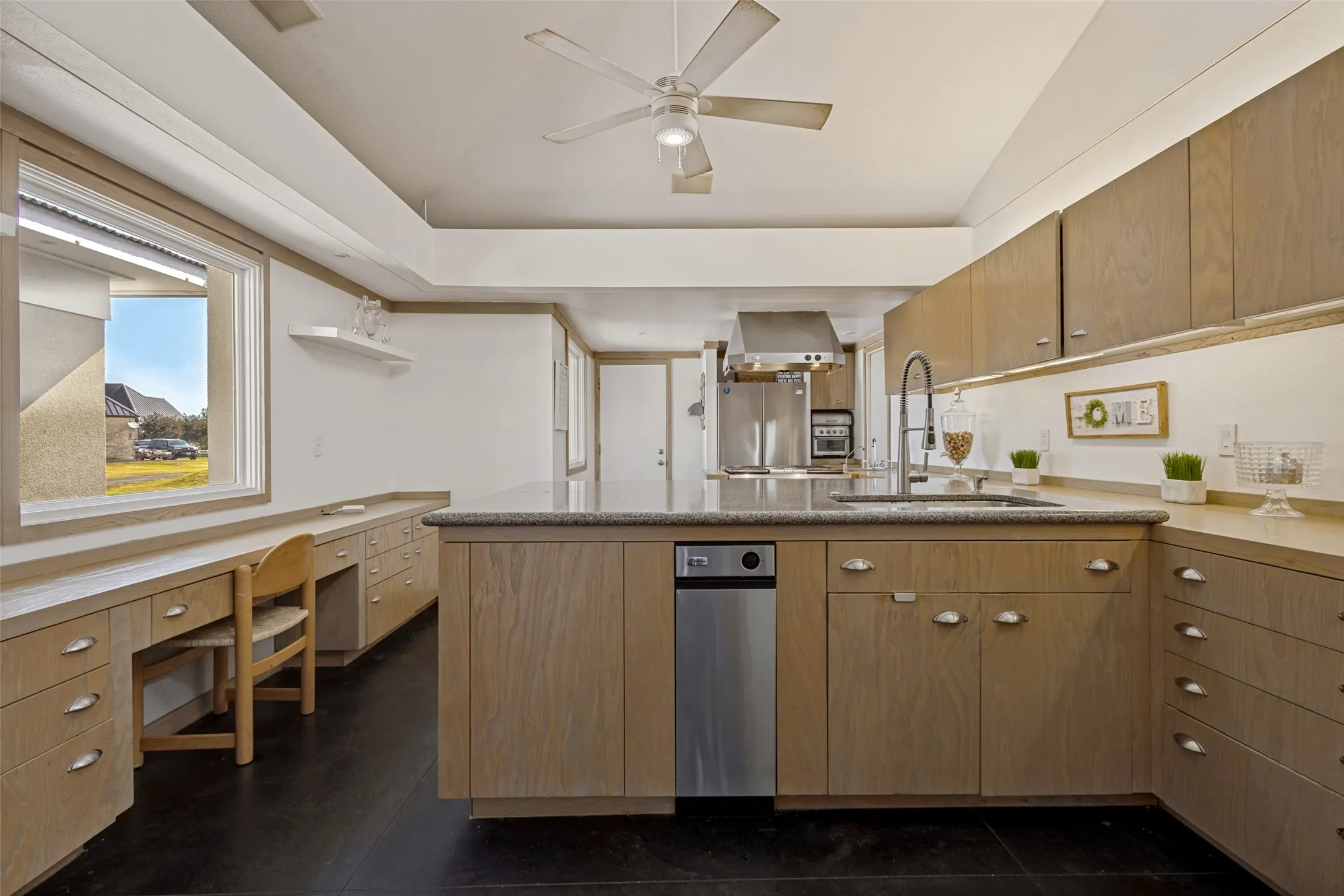 This European styled kitchen has a sleek, functional design and an abundance of cabinets and drawers.  A stainless sink overlooks the rest of the kitchen with and a stainless trash compactor is nearby.  A long wall of lower drawers located under a wide winow includes a seating space ideal for meal planning or grabbing a quick snack.