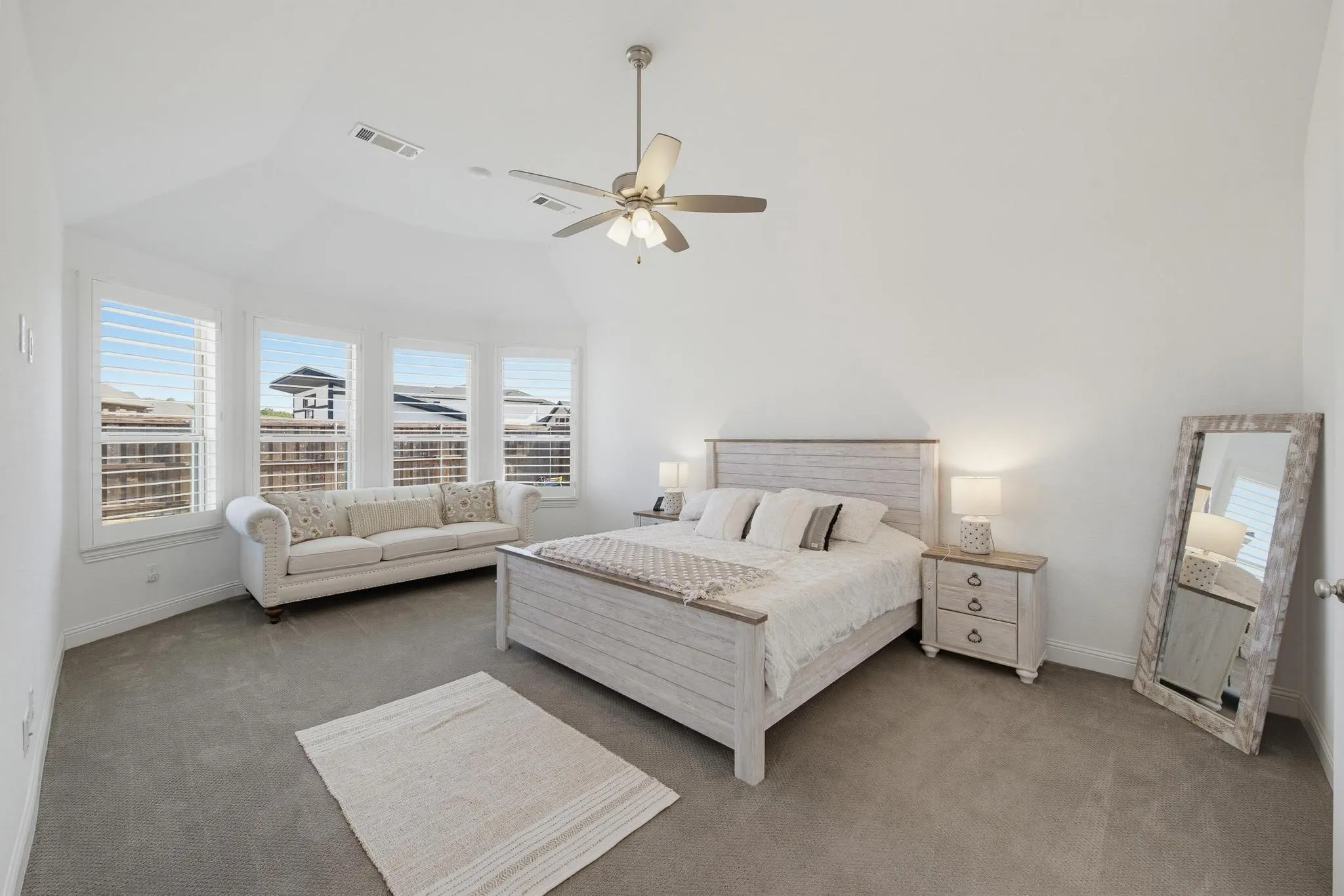 Vaulted ceiling with a ceiling fan, bay window with plantation shutters, and gray carpet flooring