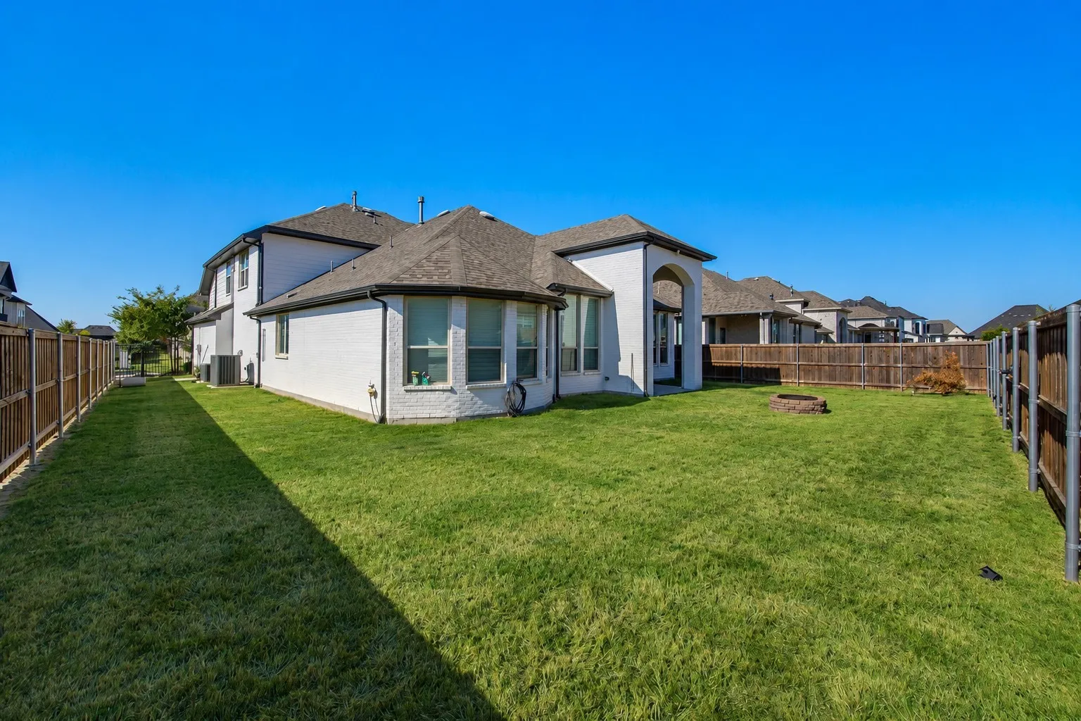 Expansive backyard featuring a manicured lawn, full perimeter fencing, and a built-in fire pit