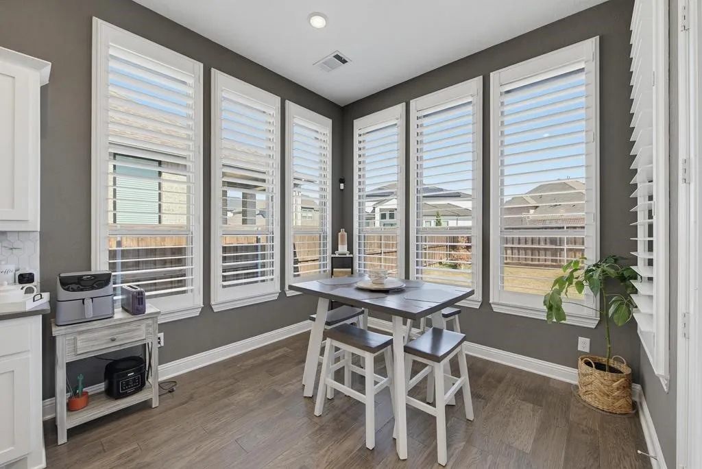 Multiple large windows with white louvered shutters, wood-finish flooring, recessed ceiling lighting, and a white subway tile backsplash