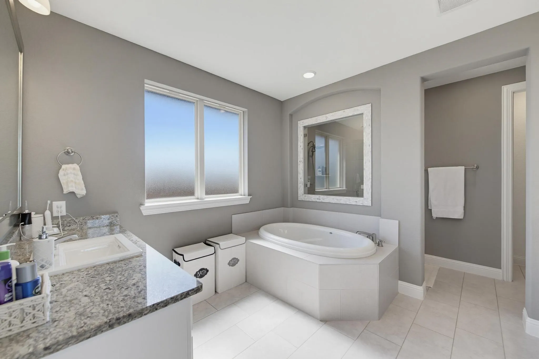 Spacious bathroom featuring a built-in soaking tub, a vanity with an integrated sink and stone-finish countertop, and tiled flooring