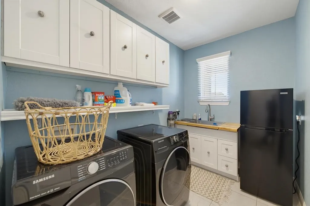 White shaker-style upper cabinetry, built-in shelving, a single-basin sink with a chrome faucet, light wood-finish countertop, and white lower cabinetry