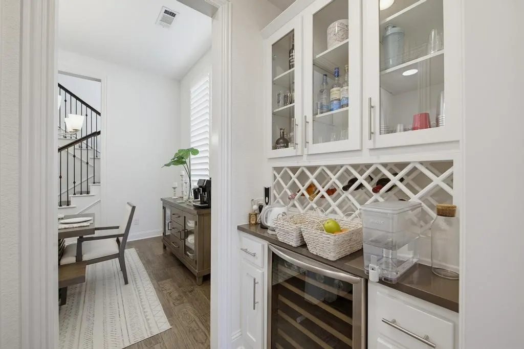 Built-in beverage bar with glass-front cabinetry, integrated wine storage, under-counter beverage refrigerator, and dark countertop