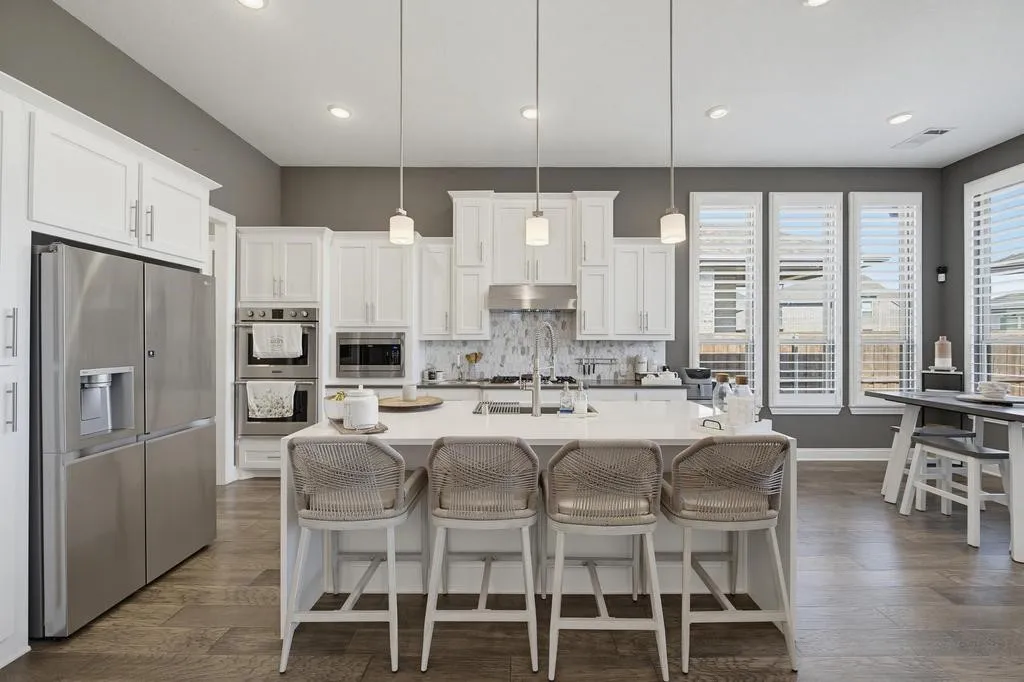 Modern kitchen featuring stainless steel appliances, white cabinetry, a large center island, pendant lighting, and wood-finish flooring