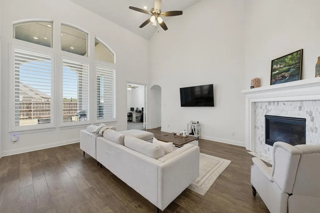 Vaulted ceiling, wood-finish flooring, tall windows with plantation shutters, fireplace with tile surround, and an arched doorway
