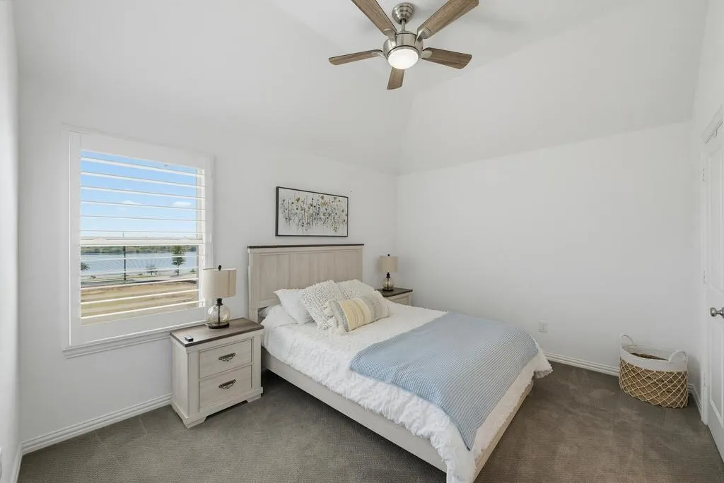 Vaulted ceiling featuring a ceiling fan, window with plantation shutters, and soft gray carpeting