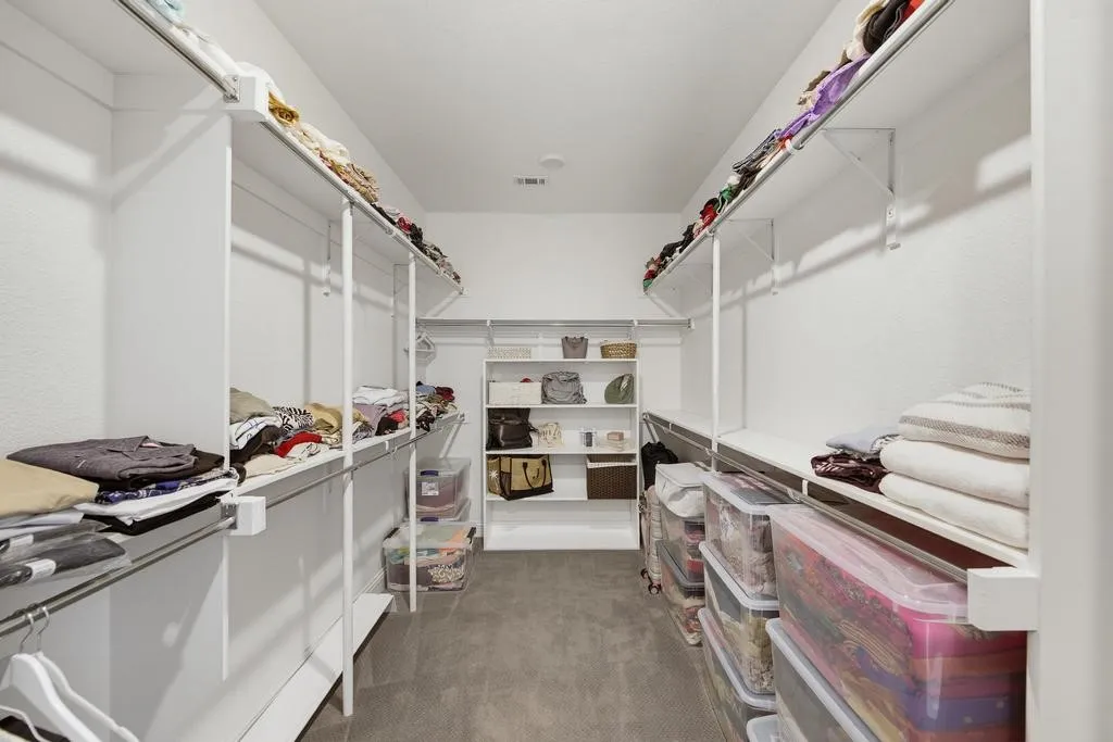 Walk-in closet with carpet flooring, white shelving, and hanging rods