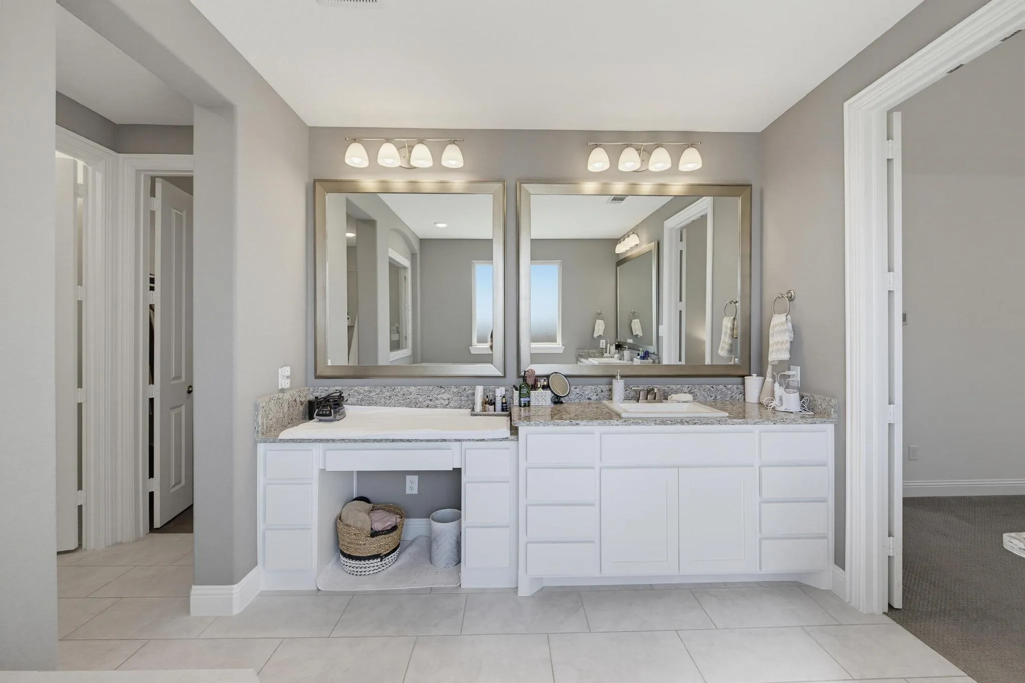 Dual vanity with granite countertops, integrated sinks, white cabinetry, and large framed mirrors with sconce lighting