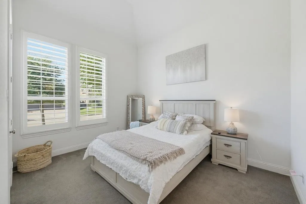 Vaulted ceiling, dual windows with plantation shutters, gray carpeting, and a built-in nightstand with drawer storage