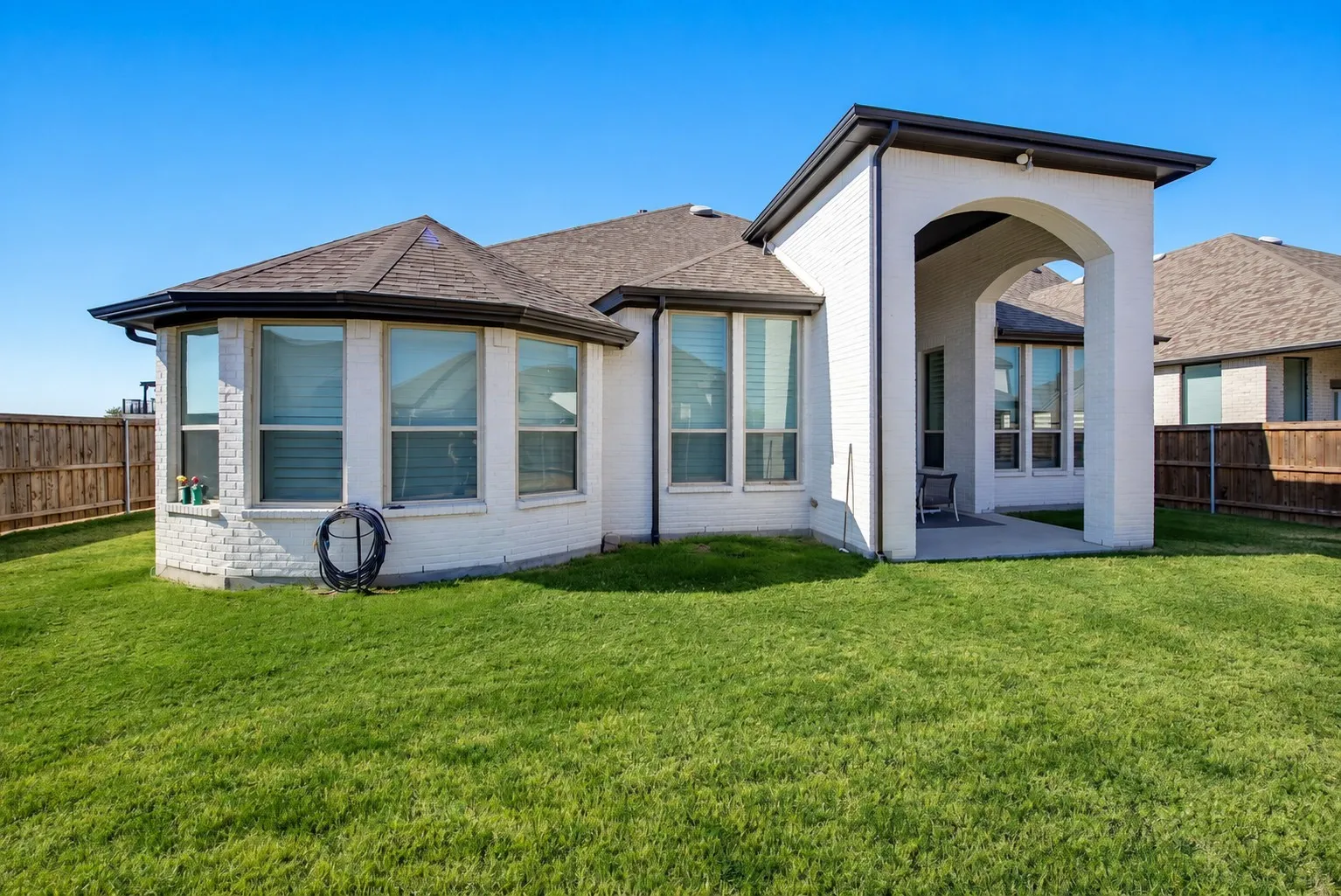 White brick exterior with dark trim, featuring multiple large windows and a covered patio