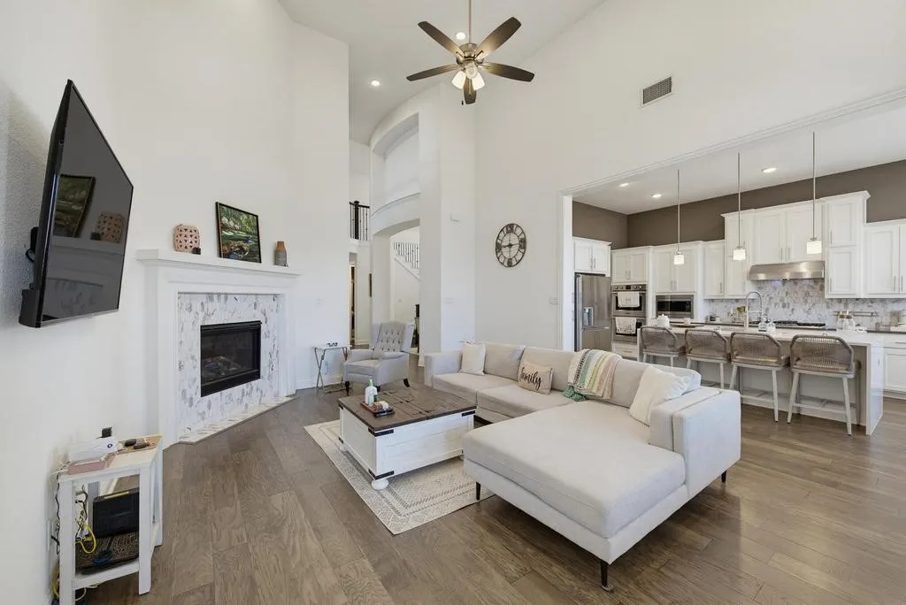 Vaulted ceilings, wood-finish flooring, a tile-surround fireplace, and a kitchen with white cabinetry and stainless steel appliances