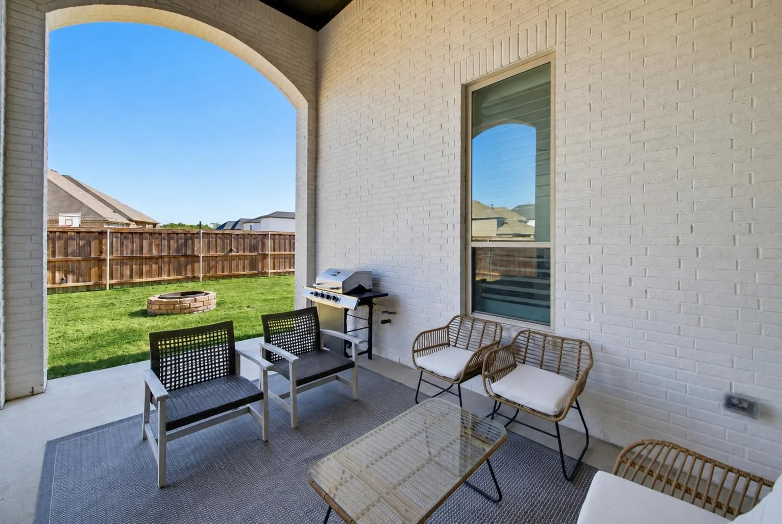 Covered patio with an arched opening, white brick exterior, a tall window, a concrete patio surface, and a fenced backyard