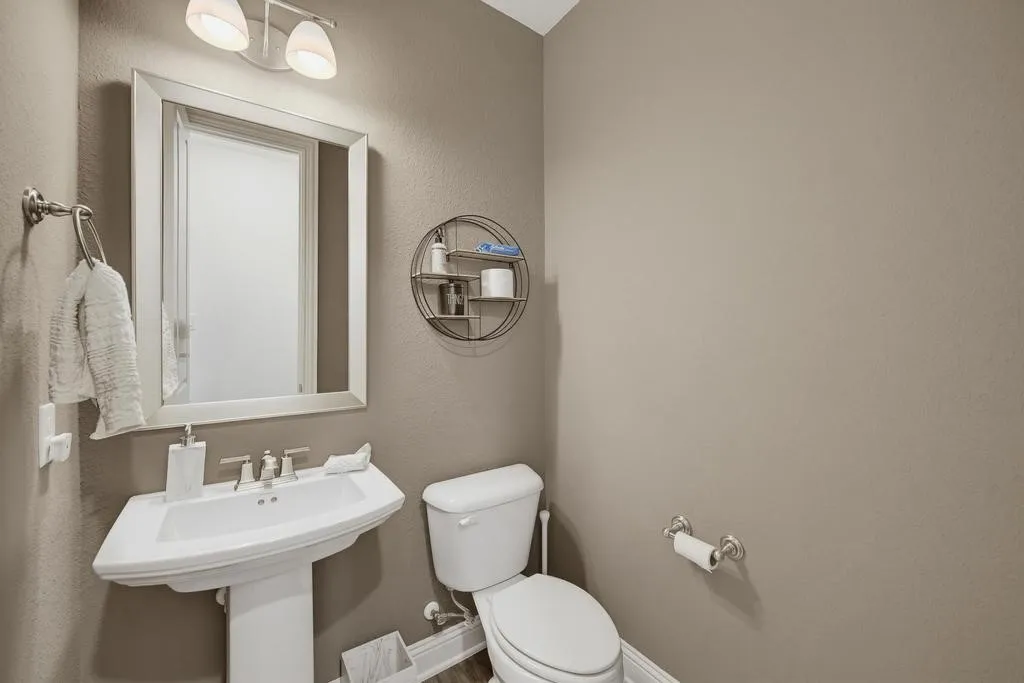 Pedestal sink with a polished chrome faucet, framed mirror, and wall-mounted light fixture