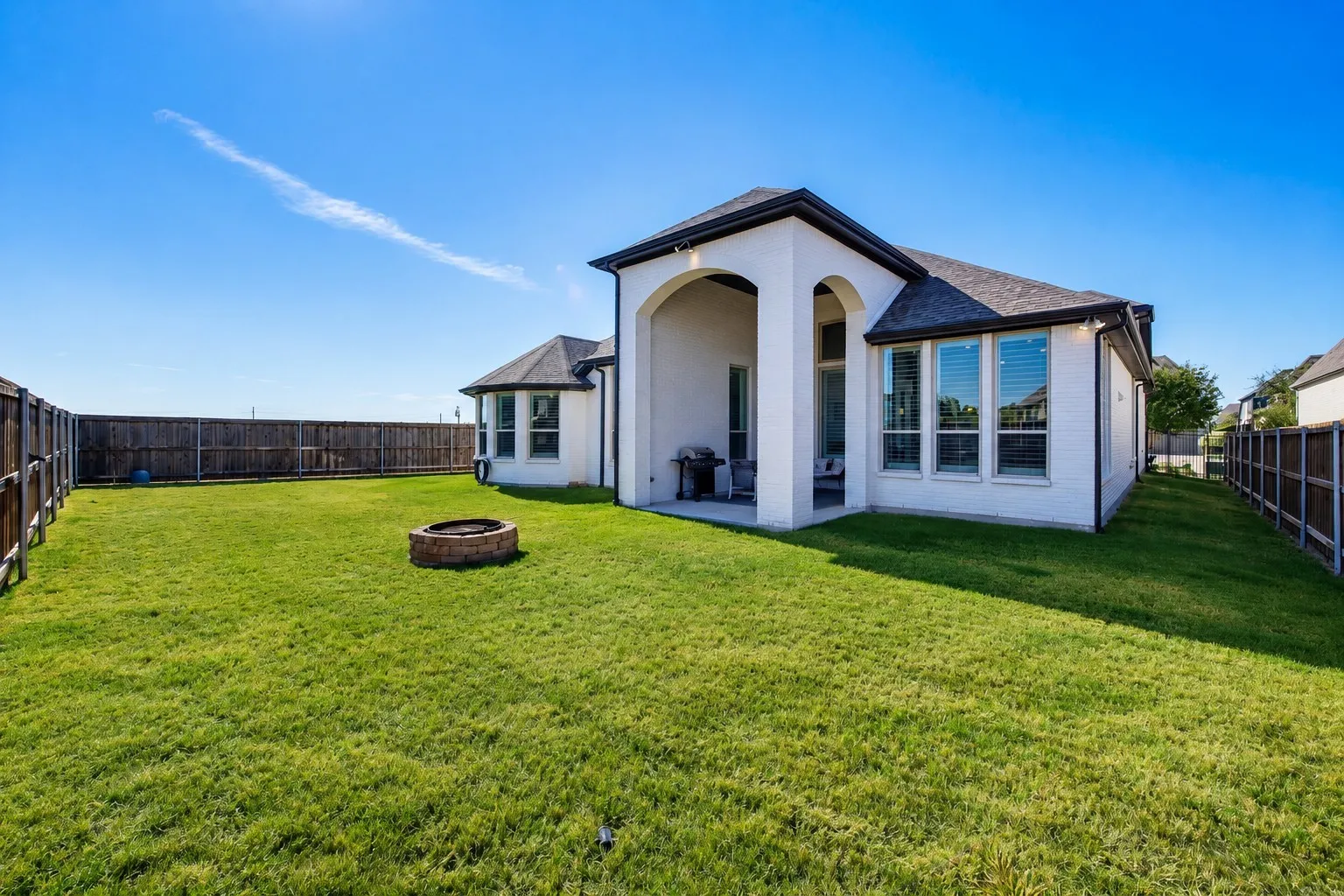 Expansive backyard with a manicured lawn, full wood fencing, and a built-in fire pit