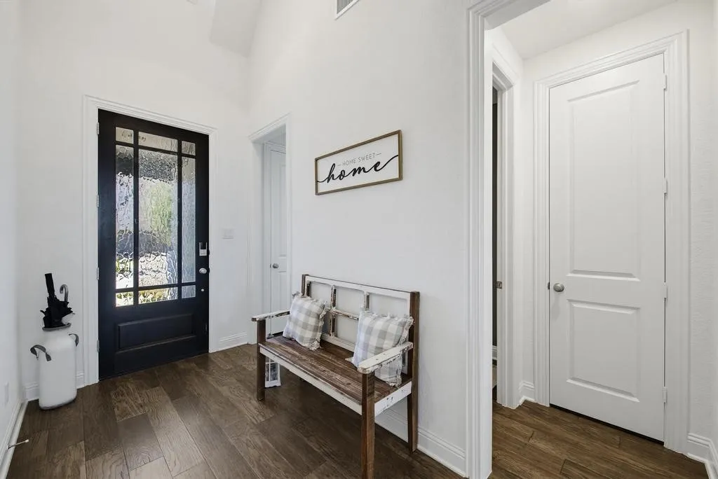 Vaulted ceiling with a dark wood-finish entry door featuring decorative glass panels, complemented by wood-finish flooring and white interior doors