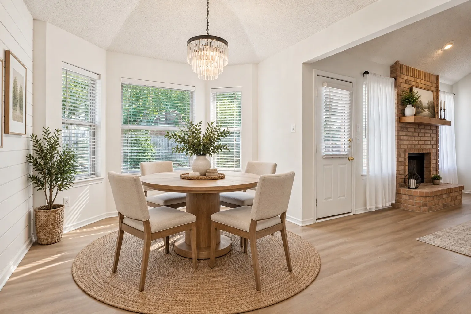 Bay window dining area with a tiered crystal chandelier, wood-finish flooring, and a brick fireplace