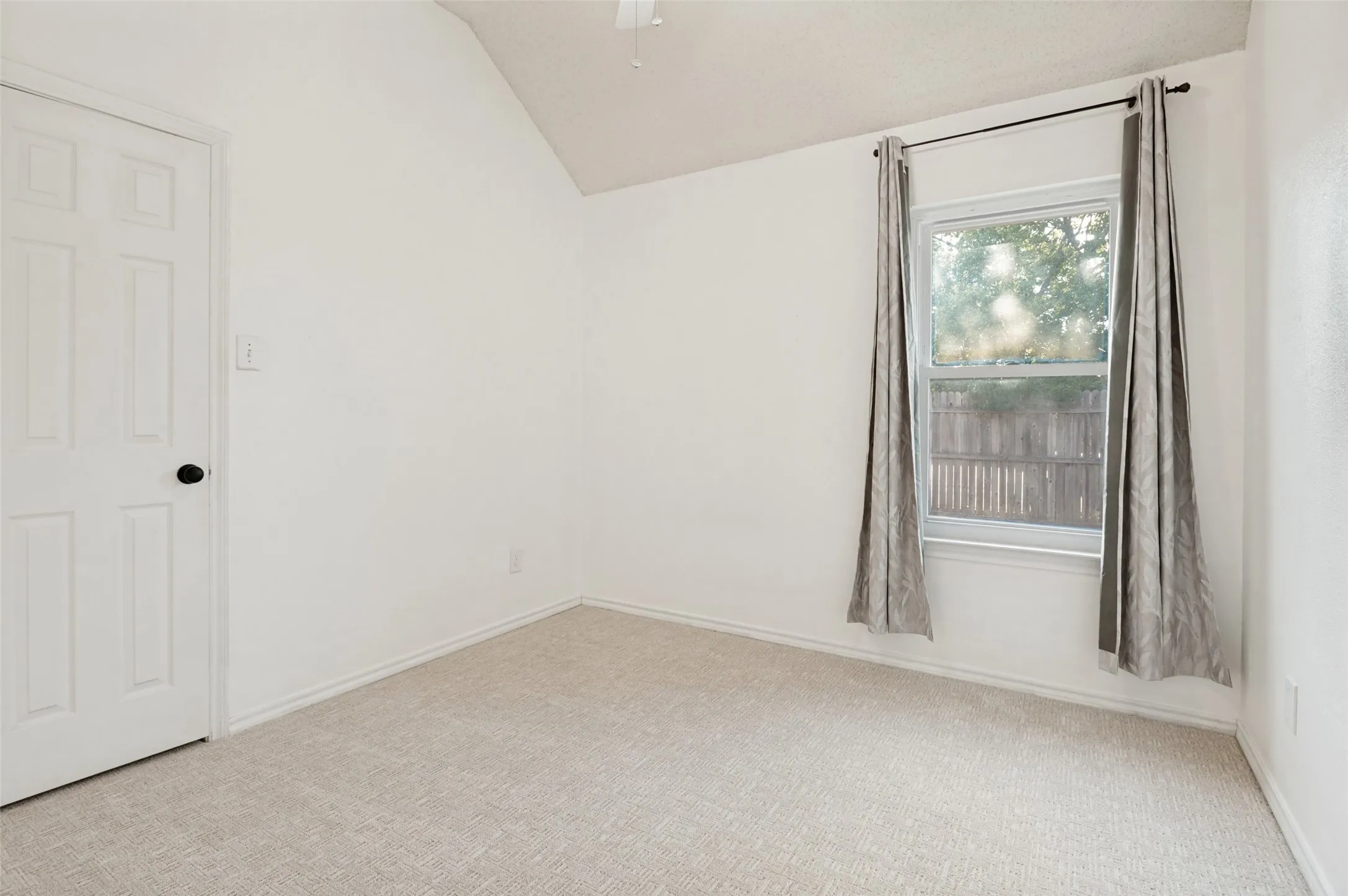 Vaulted ceiling with a ceiling fan, light-colored carpet flooring, and a single window