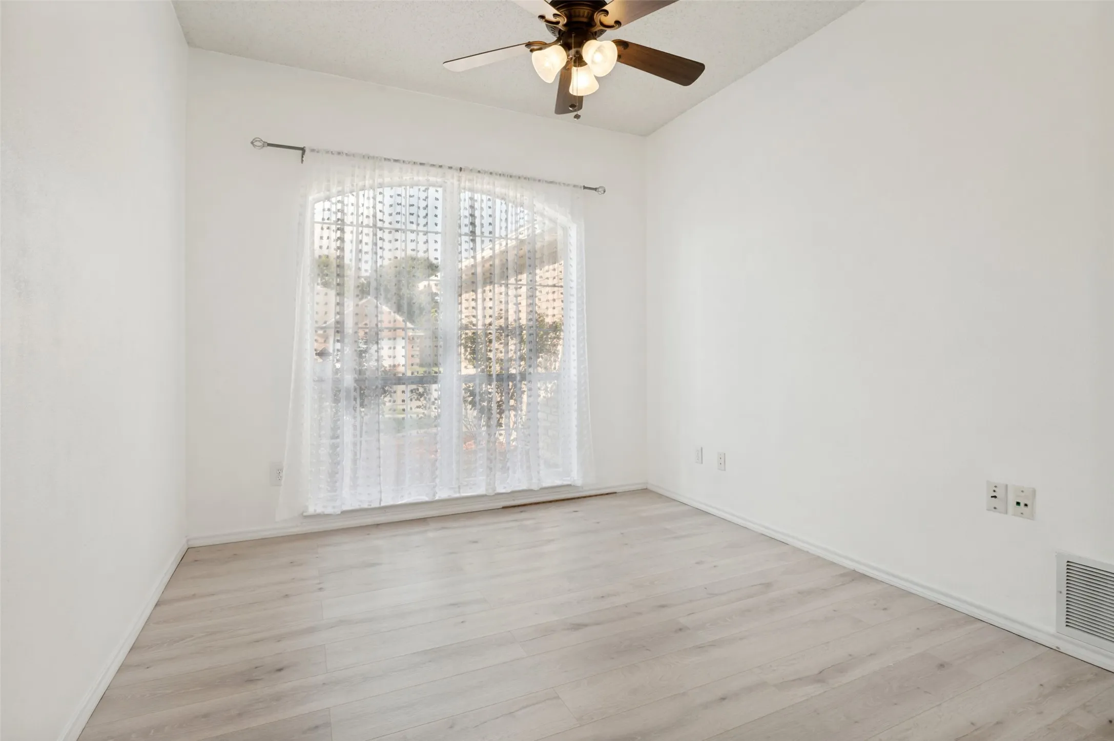 Vaulted ceiling with a ceiling fan, arched window, and wood-finish flooring