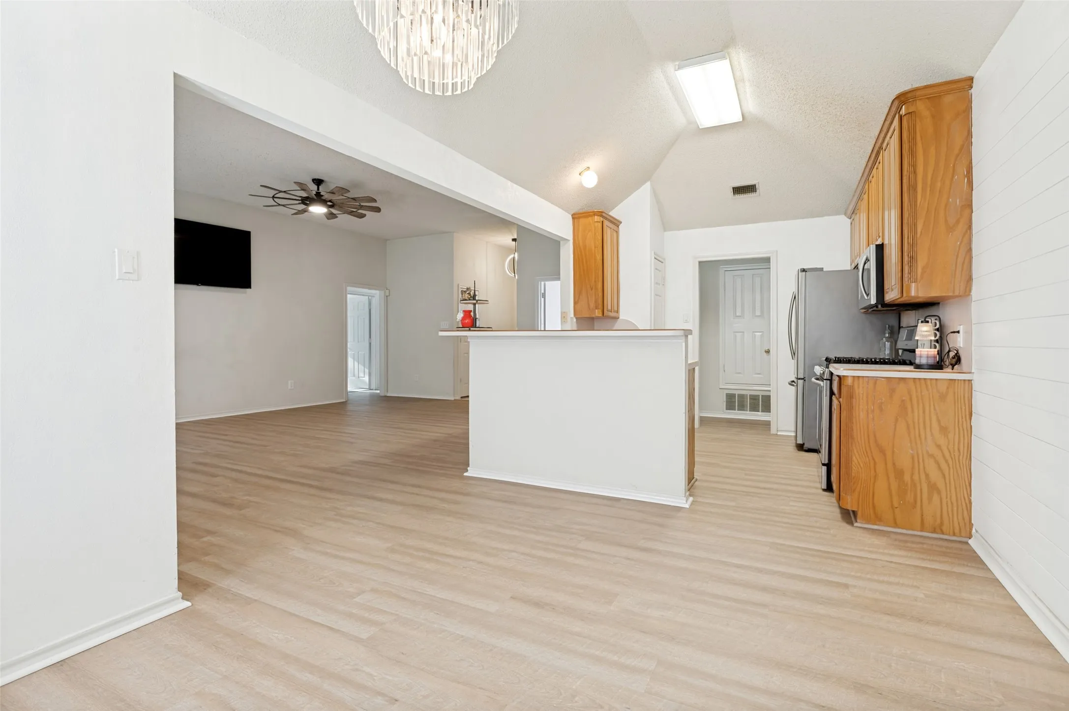 Vaulted ceiling with an overhead light fixture and skylight, wood-finish flooring, light wood cabinetry, and stainless steel appliances