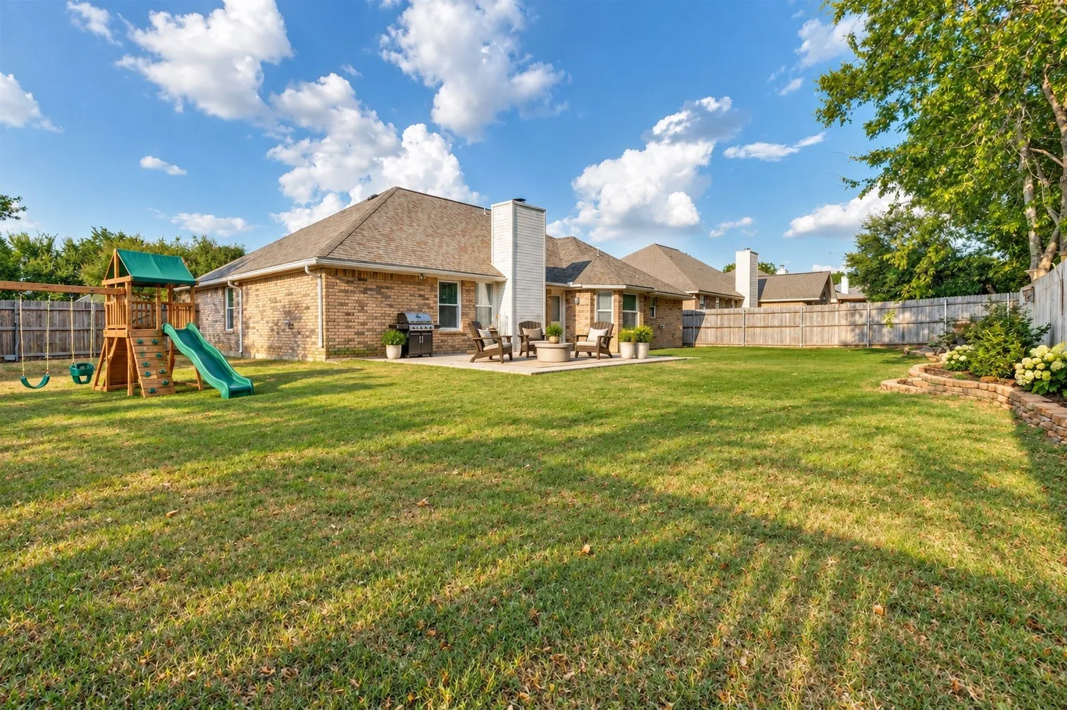Expansive green lawn with a wood privacy fence and a stone-edged planting bed