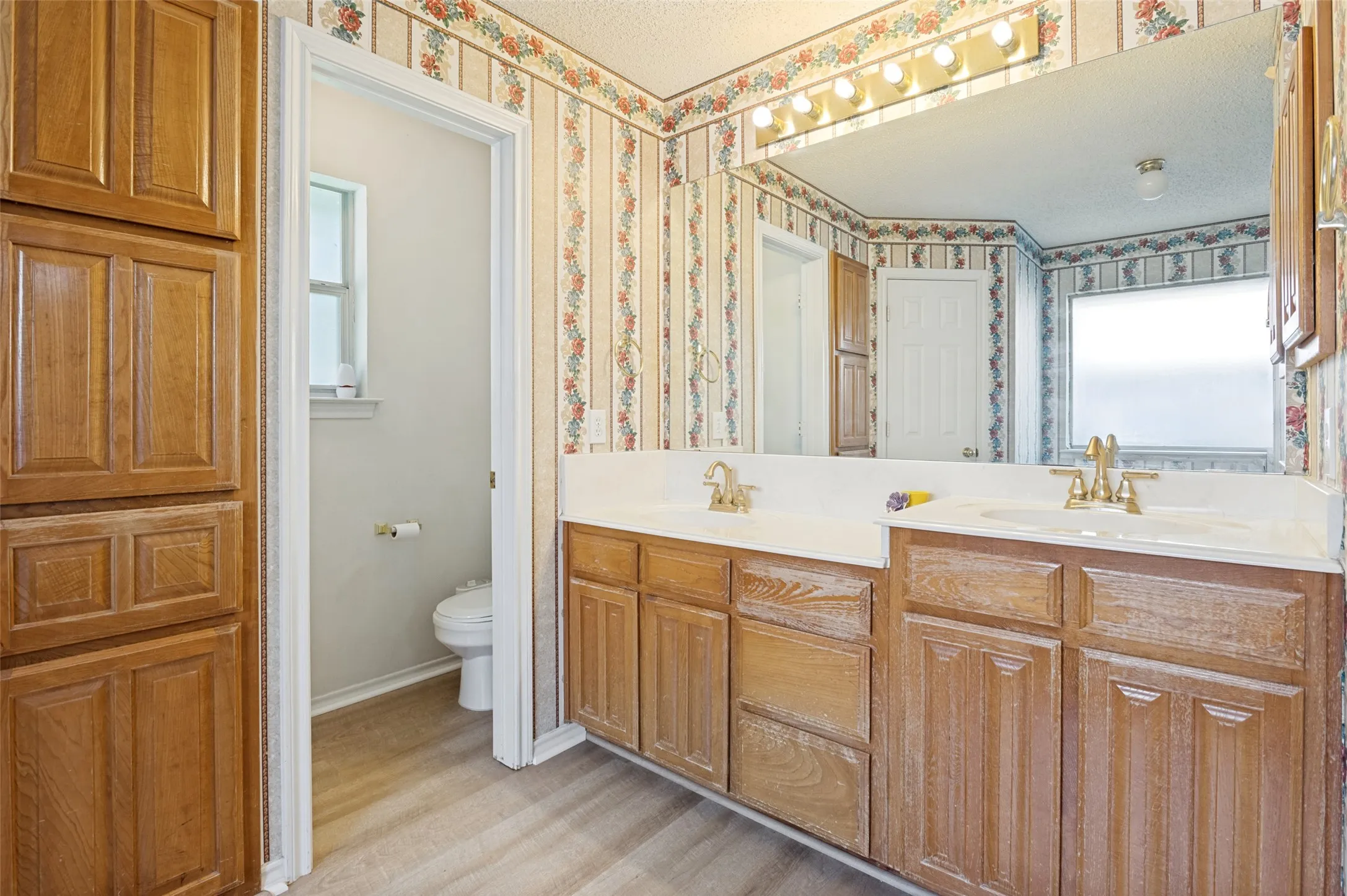 Wood-finish cabinetry, dual undermount sinks with brass-finish fixtures, and a vanity-width mirror