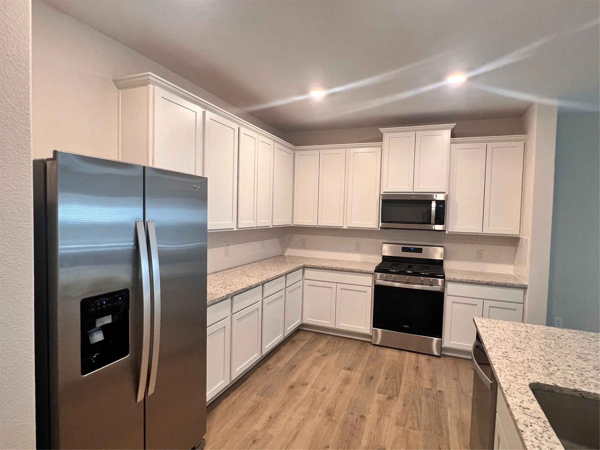 Kitchen featuring white cabinetry, light granite countertops, wood-finish flooring, and stainless steel appliances including a refrigerator, range, and microwave