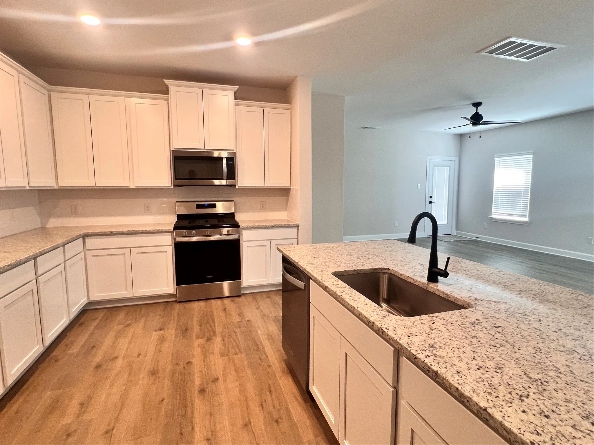 Kitchen featuring wood-finish flooring, white cabinetry, integrated stainless steel appliances, and a kitchen island with an undermount sink and matte black faucet