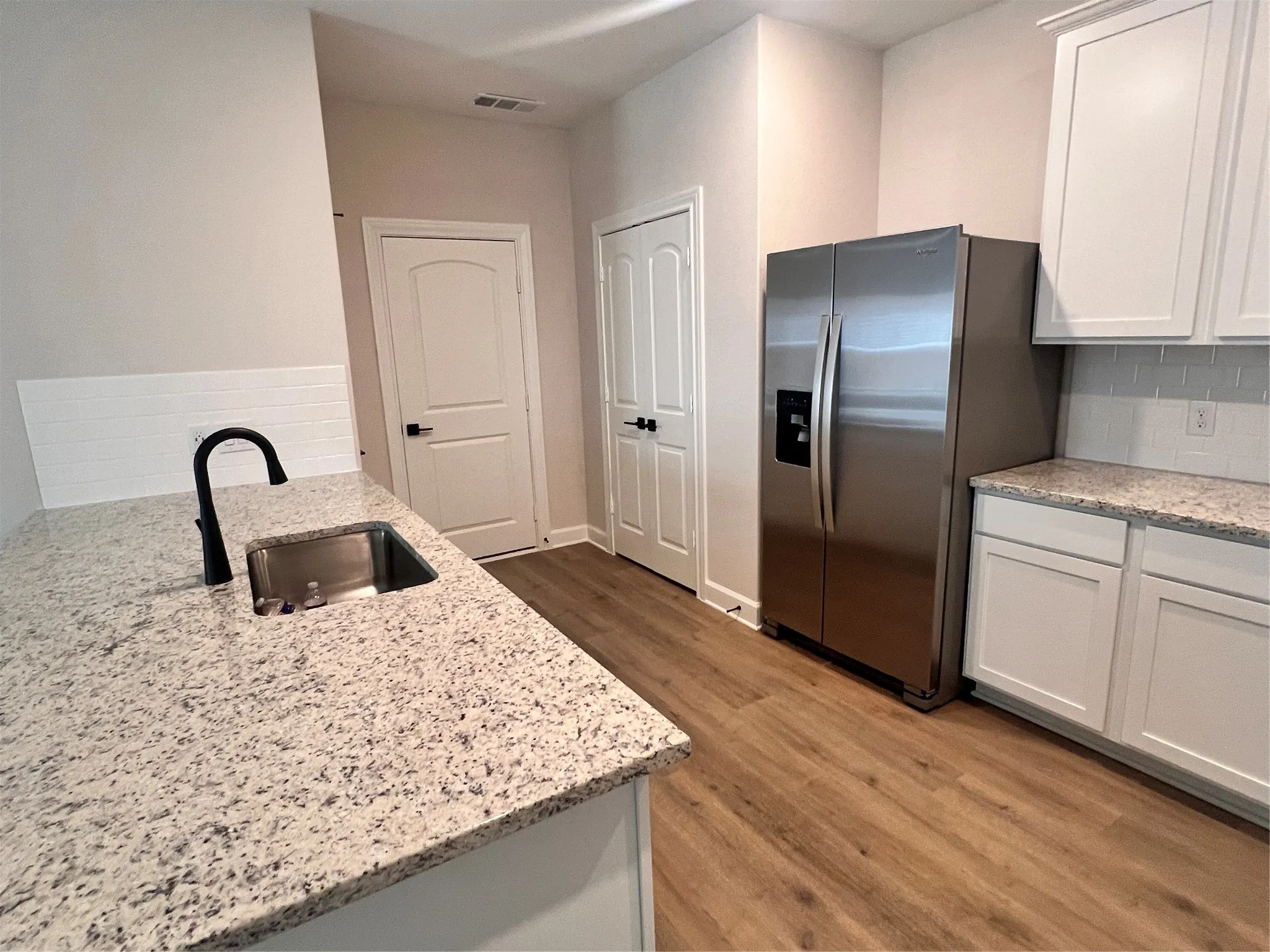 Kitchen featuring wood-finish flooring, white cabinetry, granite-style countertops, stainless steel appliances, and a subway tile backsplash