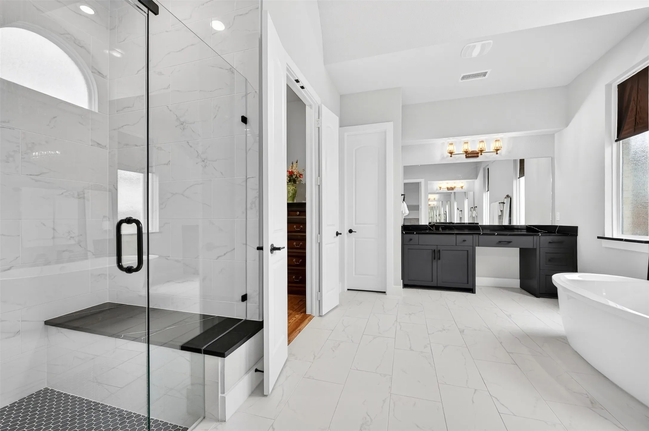 Spacious bathroom featuring a frameless glass shower with built-in bench, freestanding soaking tub, and a vanity with dual sinks and ample countertop space