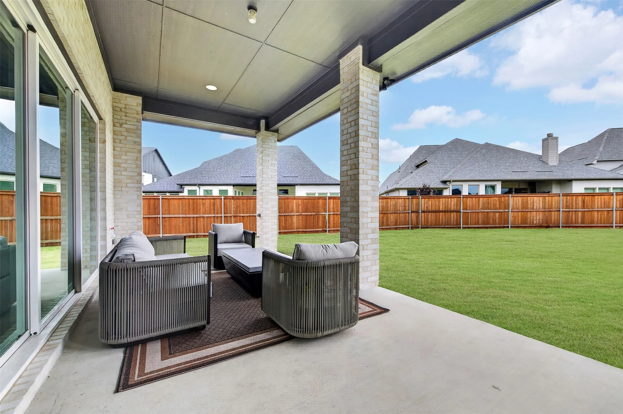 Covered patio with recessed lighting, brick columns, and direct access to a grassy yard with wood fencing