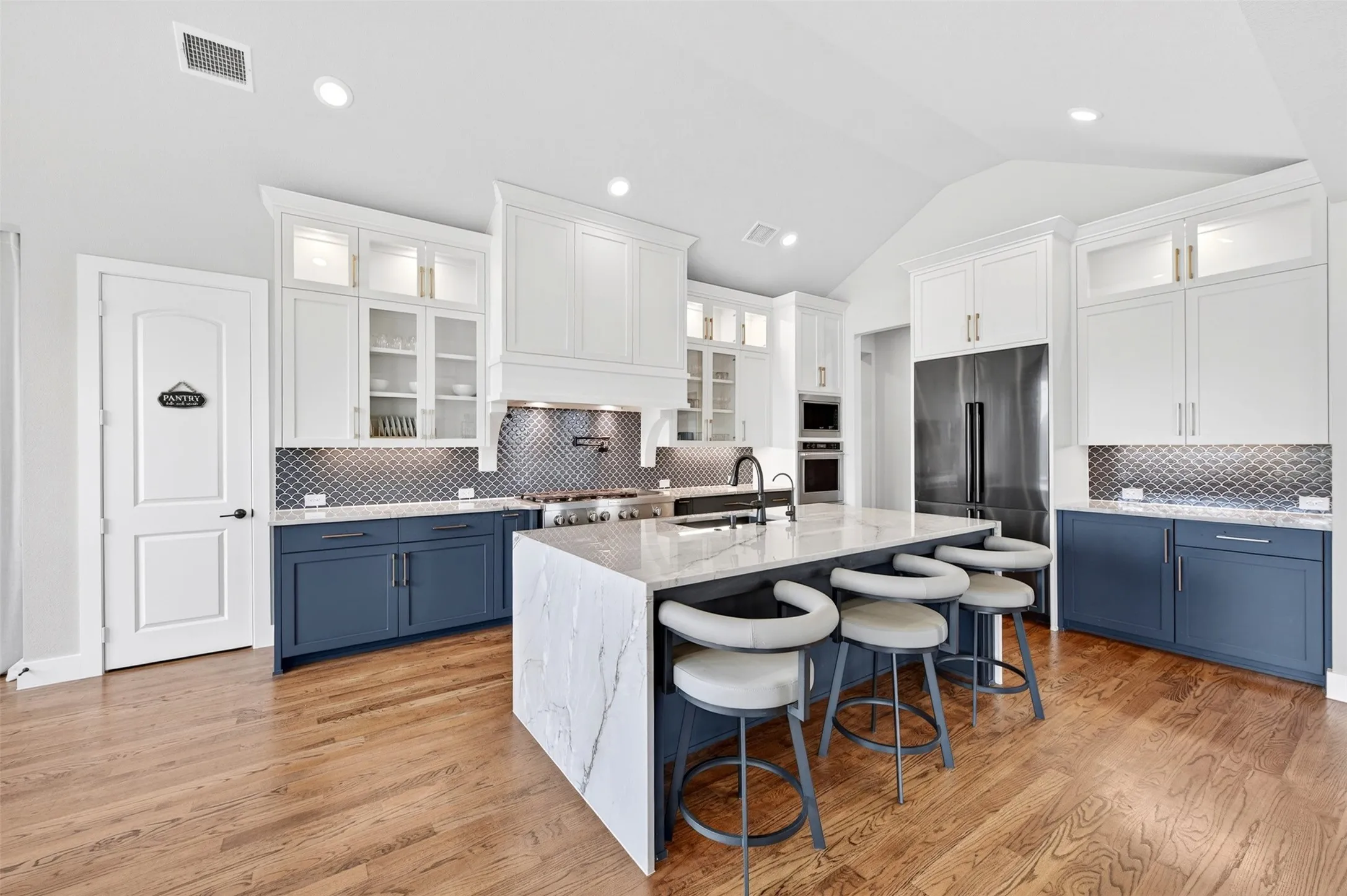 Gourmet kitchen featuring a waterfall island, stainless steel appliances, two-tone cabinetry, wood-finish flooring, and a patterned backsplash