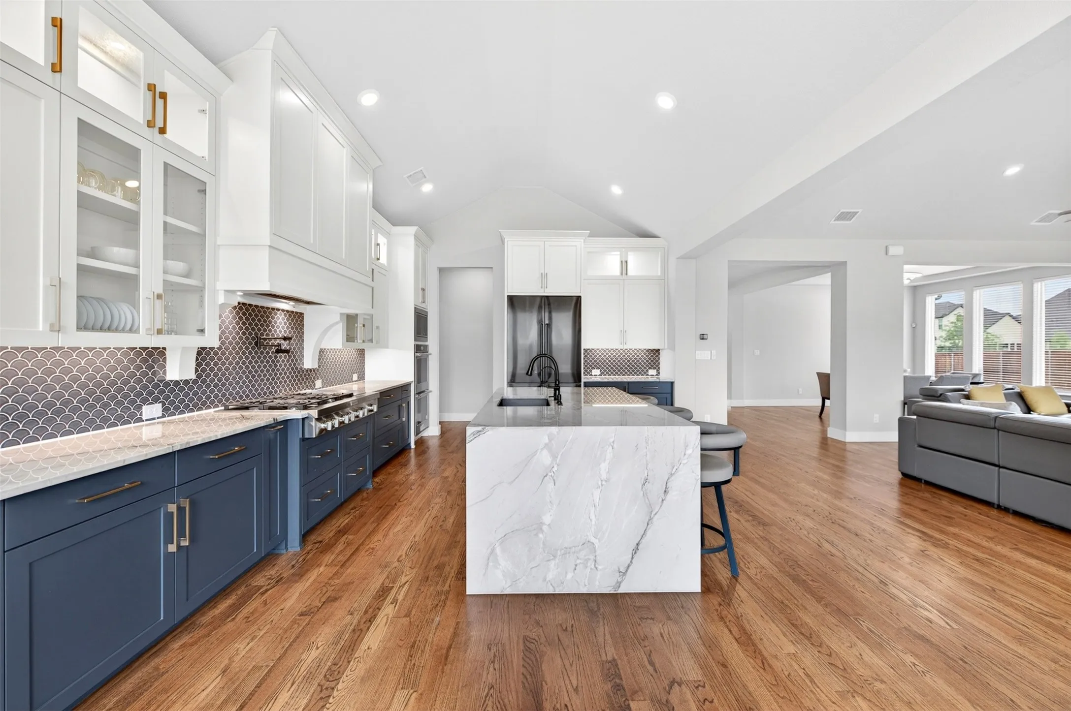 Open-concept kitchen with wood-finish flooring, two-tone cabinetry, a large waterfall island, and a decorative tile backsplash