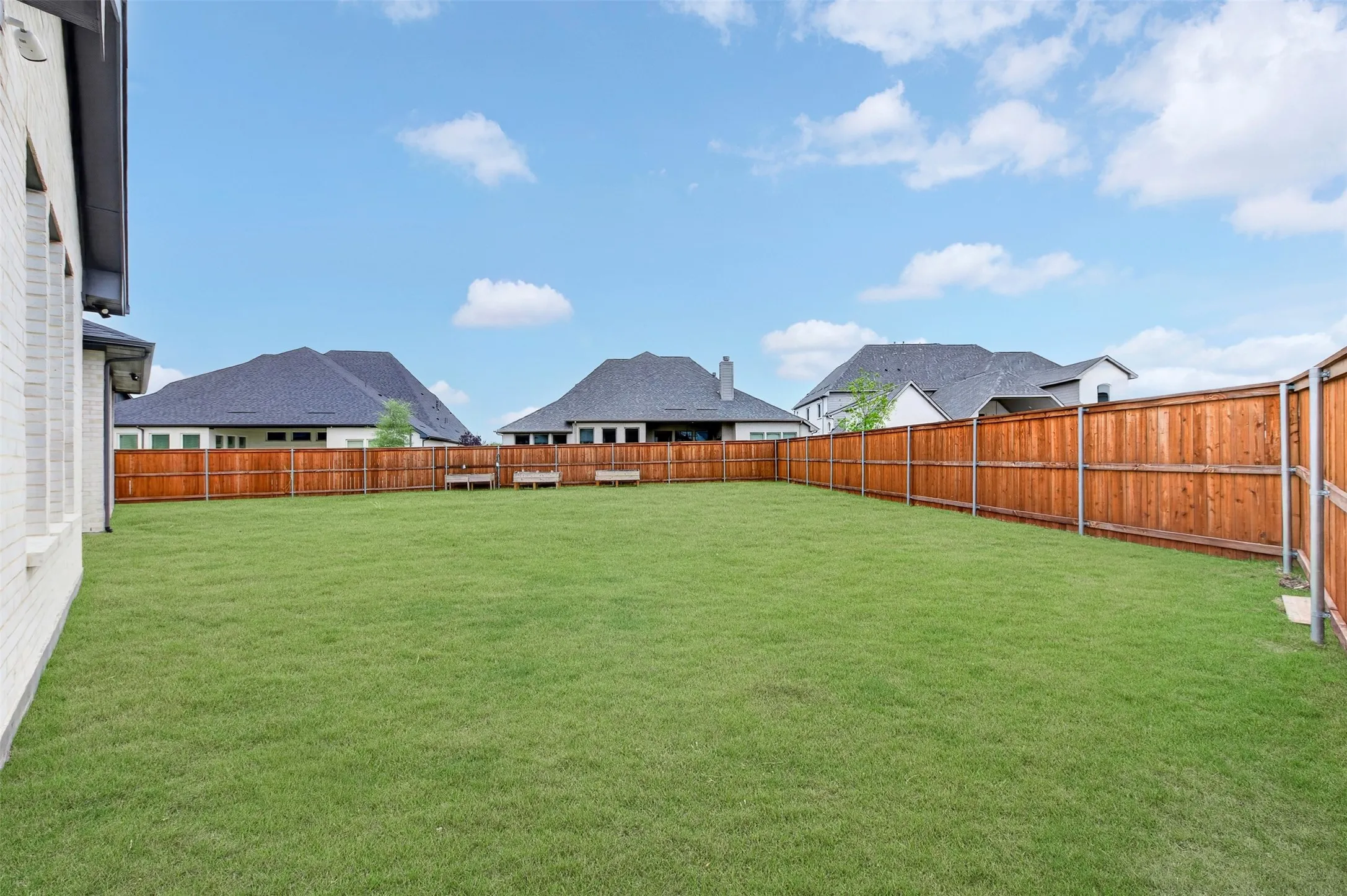 Expansive backyard featuring a manicured lawn, wood privacy fencing, and a white brick exterior