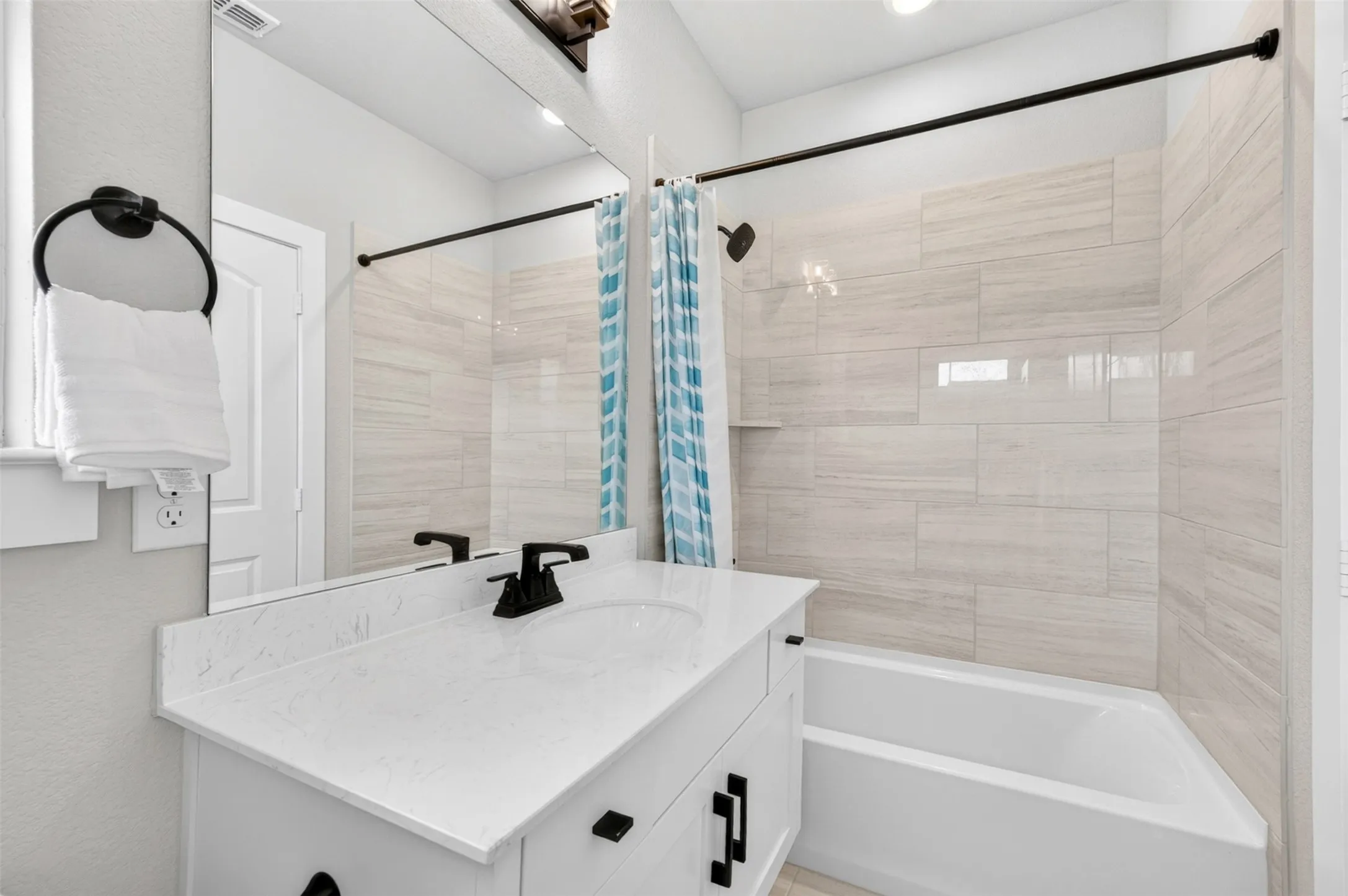 White vanity cabinet with a stone-finish countertop, single undermount sink, and matte black faucet