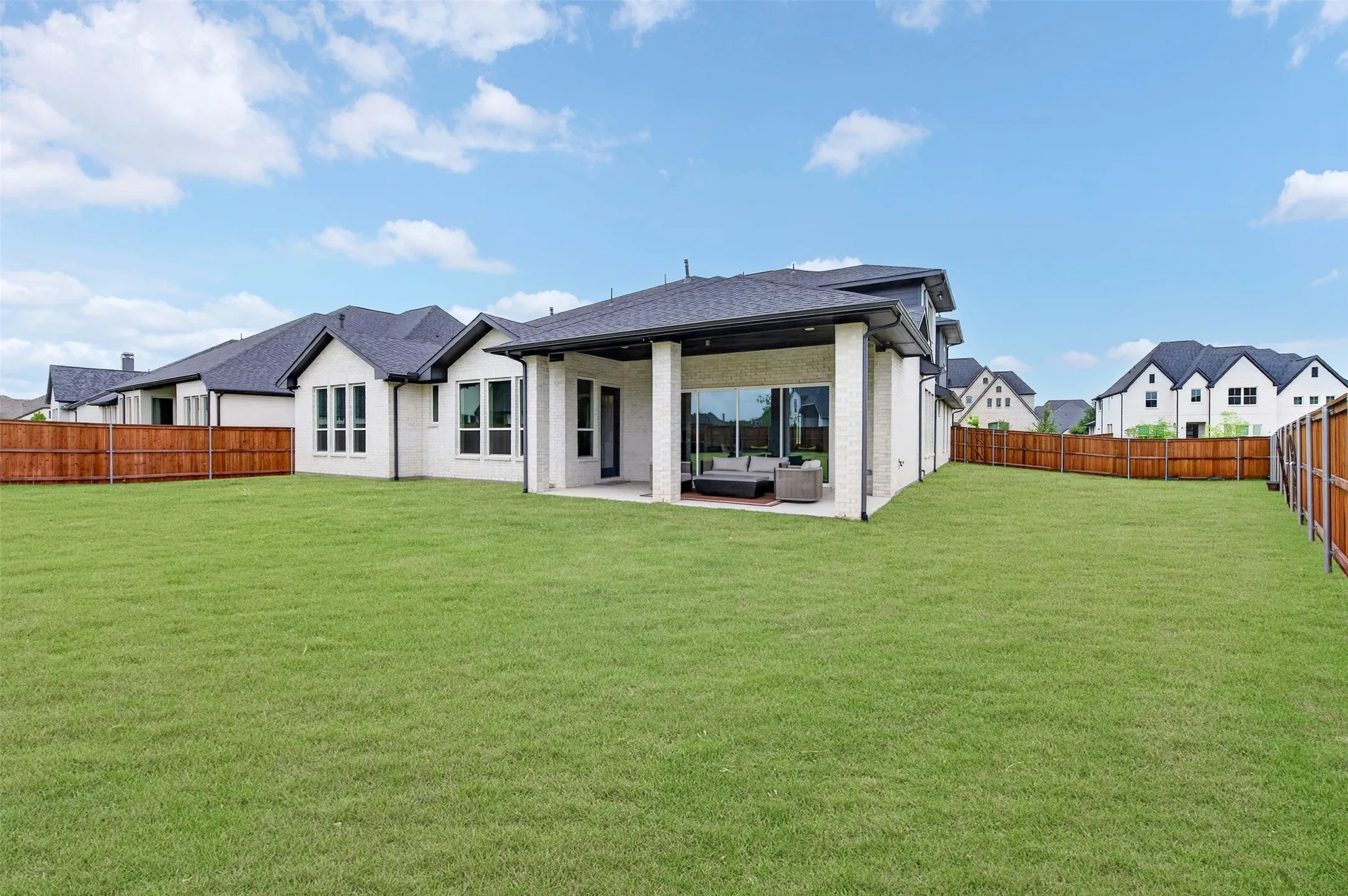 Expansive green lawn with a covered patio, large glass sliding doors, and white brick exterior
