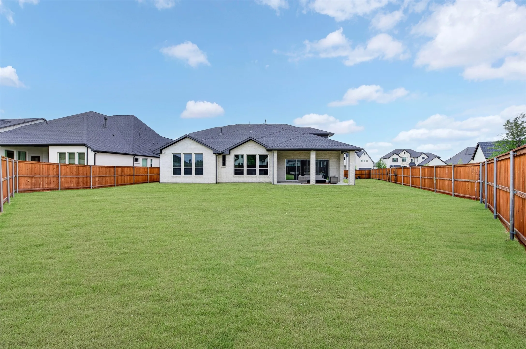 Expansive backyard with a manicured lawn, full privacy fencing, and a covered patio