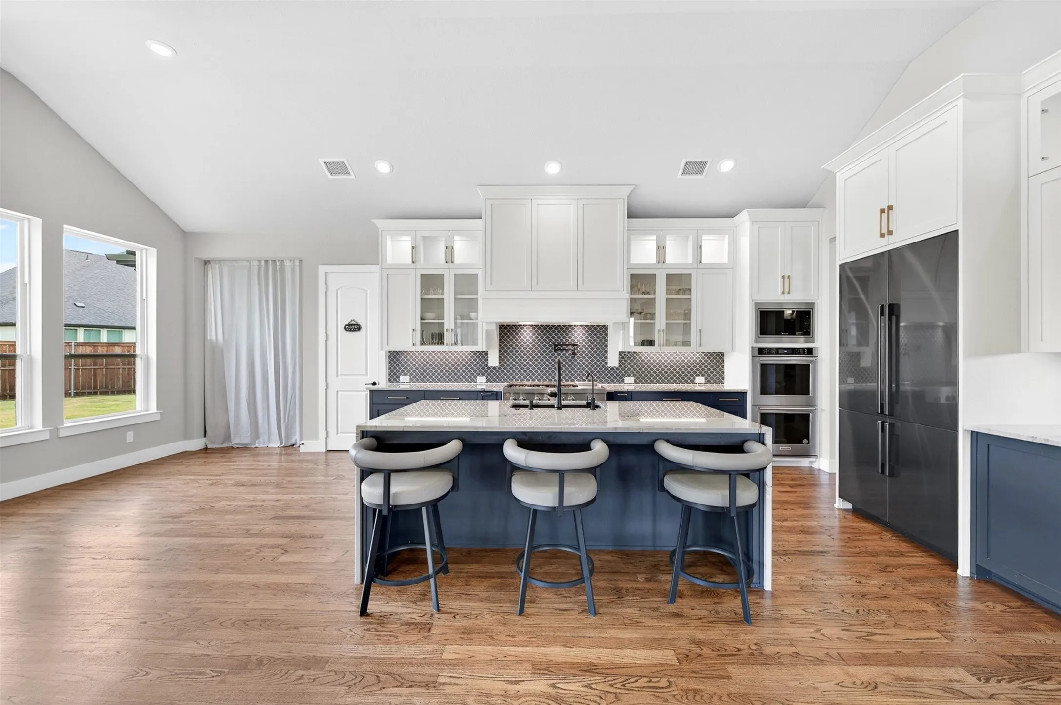 Gourmet kitchen with a large island, stainless steel appliances, custom cabinetry, and wood-finish flooring