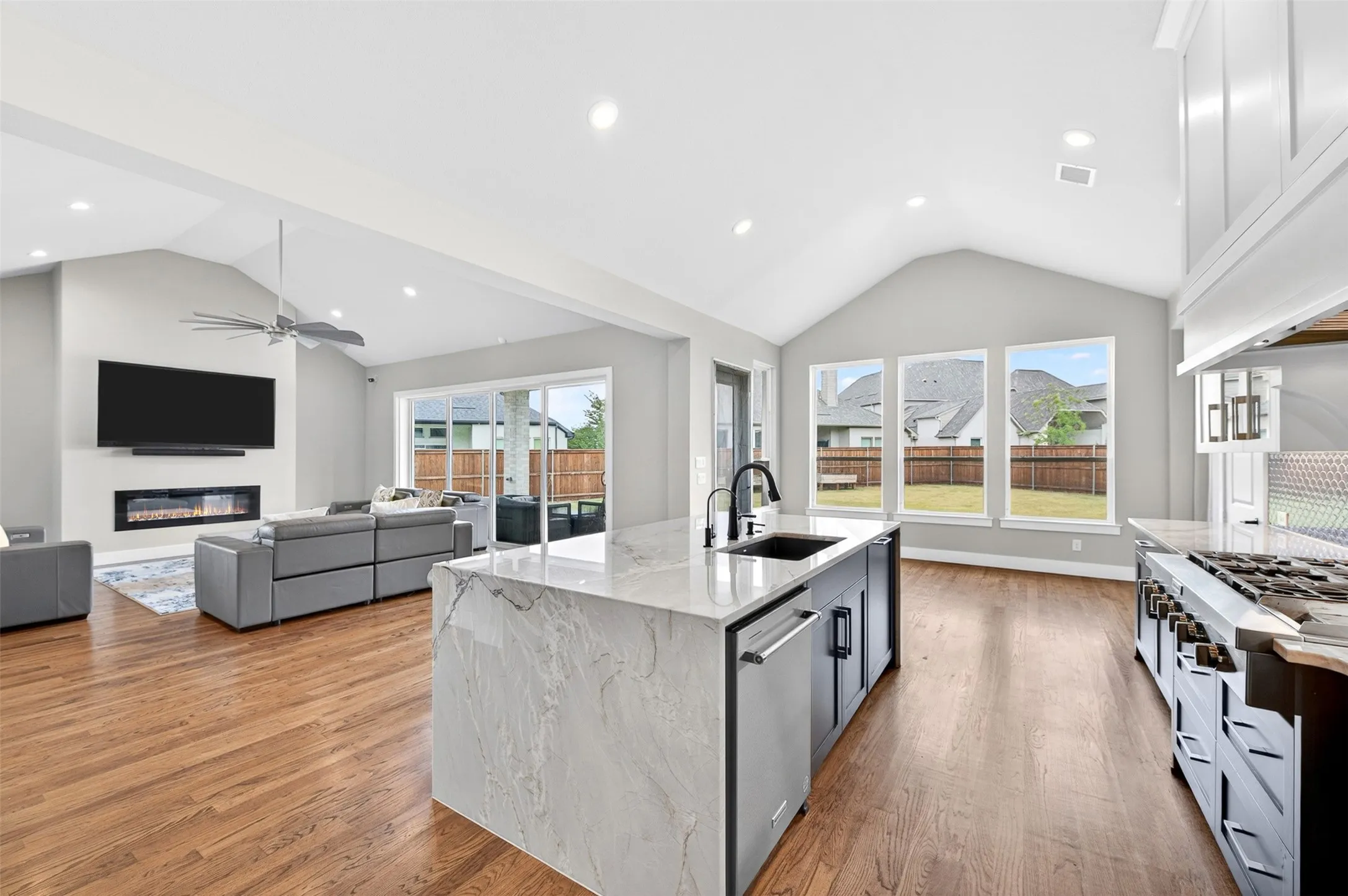Vaulted ceilings, wood-finish flooring, a kitchen island with integrated sink, a built-in fireplace, and sliding glass doors to the backyard
