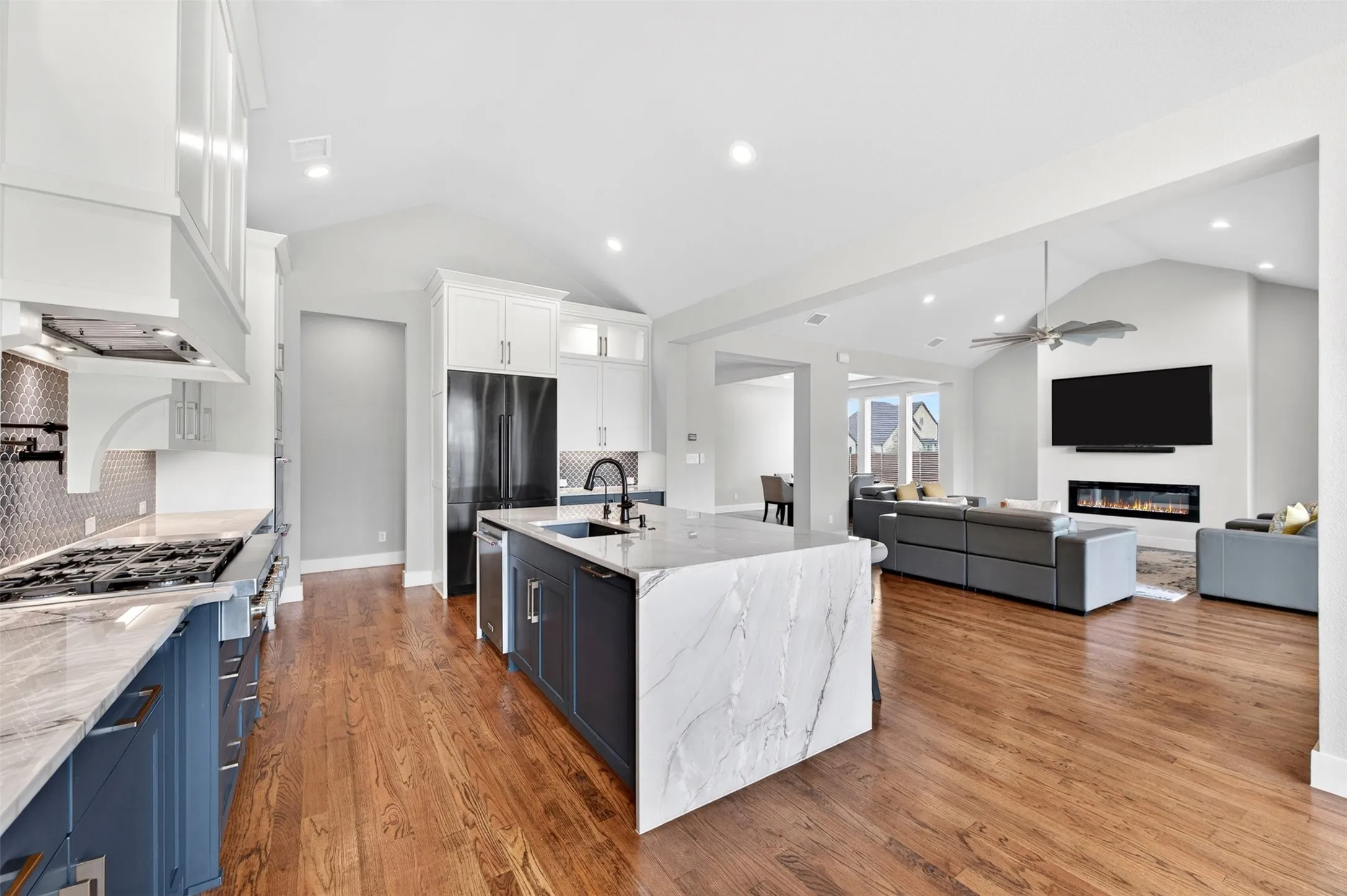 Gourmet kitchen with an expansive island featuring a waterfall countertop, a gas range with a custom hood, and a geometric tile backsplash