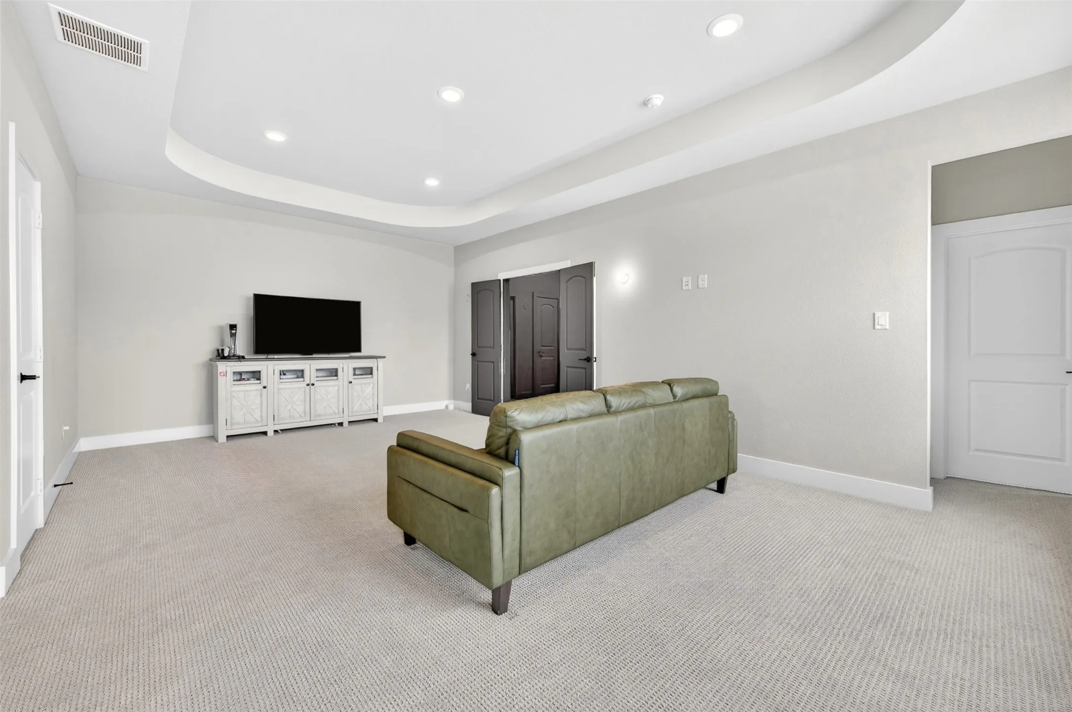 Recessed lighting, curved tray ceiling, light neutral-toned carpeting, and light wall finishes