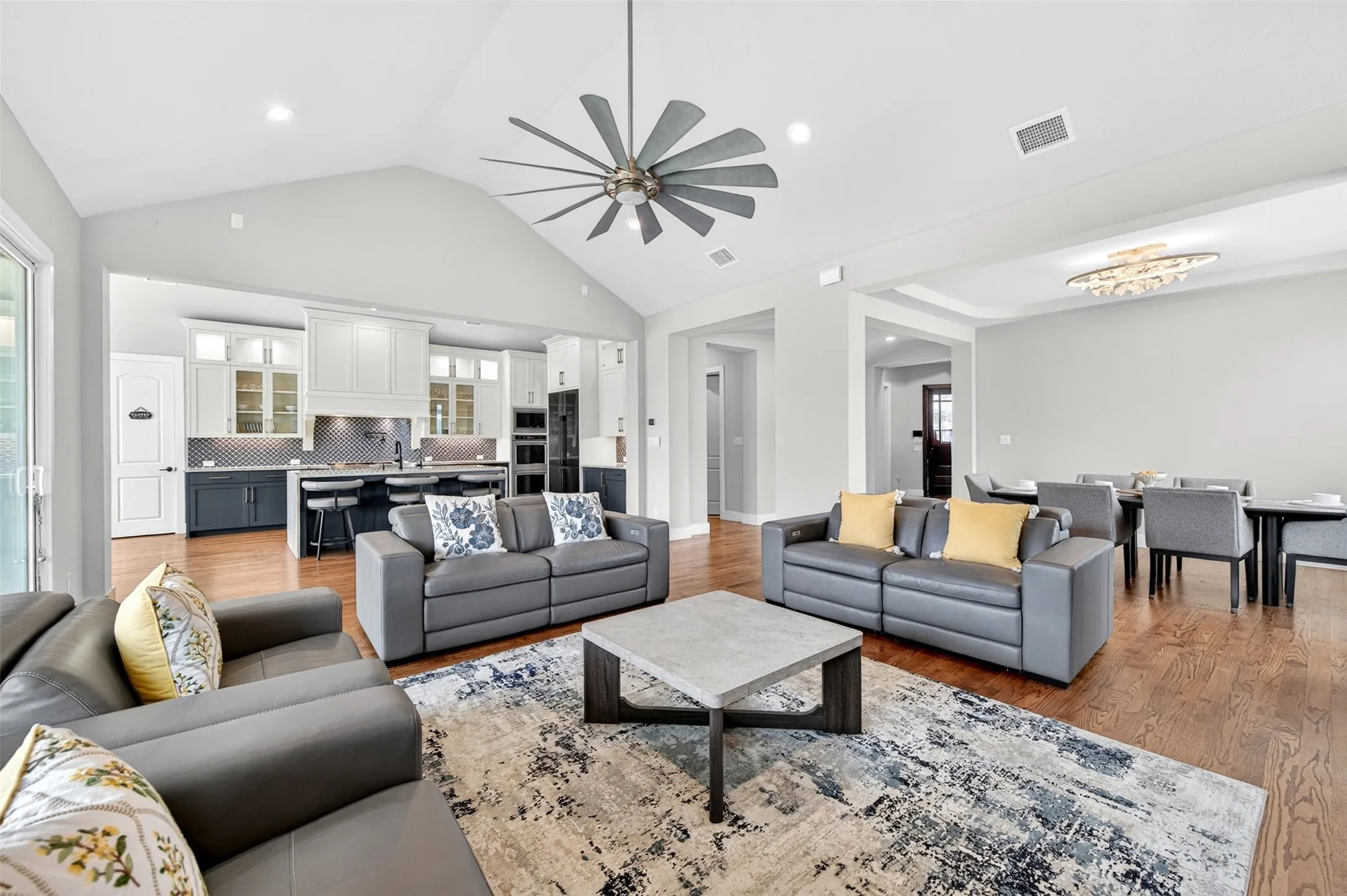 Vaulted ceilings, wood-finish flooring, recessed lighting, ceiling fan, and a kitchen with an island