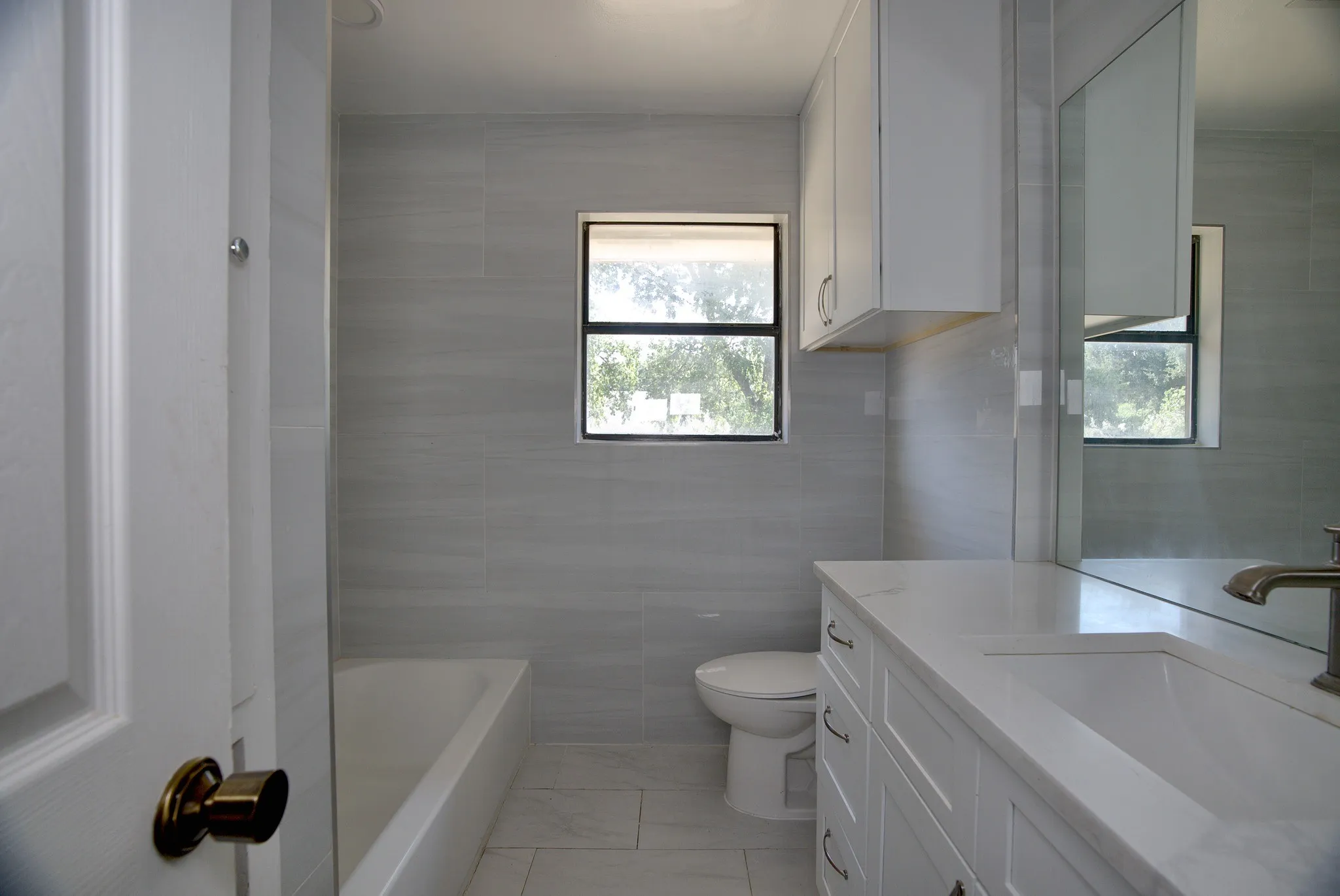Full bathroom featuring light gray tiled walls, a white bathtub, a single vanity with a white countertop and integrated sink, white cabinetry, and a window