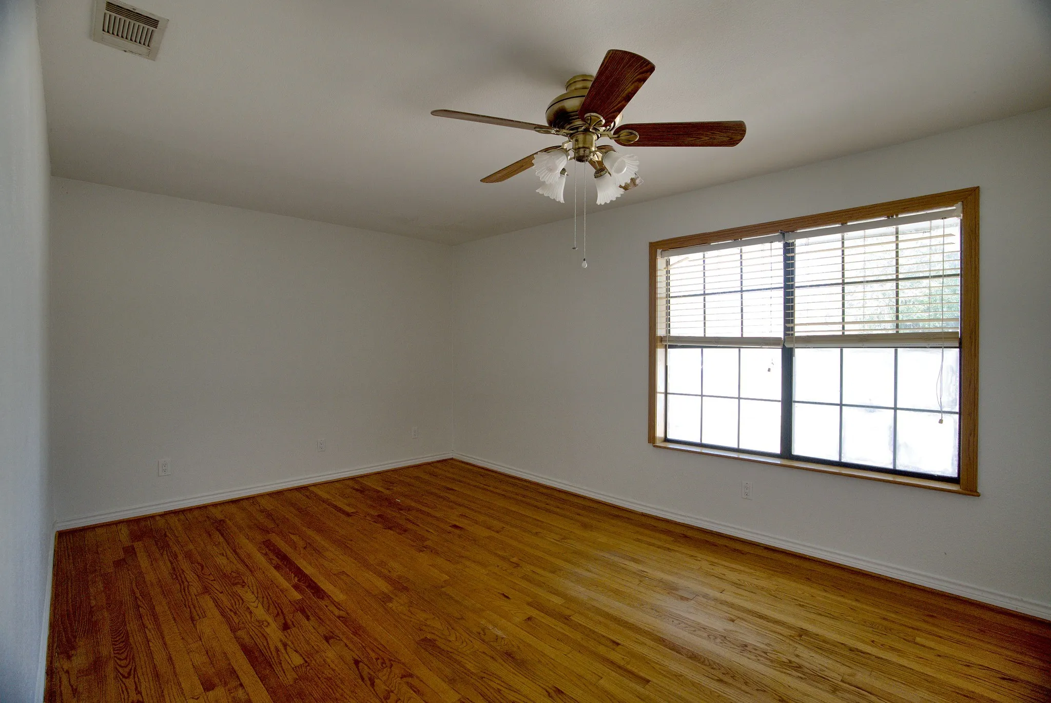 Hardwood flooring, ceiling fan with integrated lighting, window with horizontal blinds, and white wall finishes