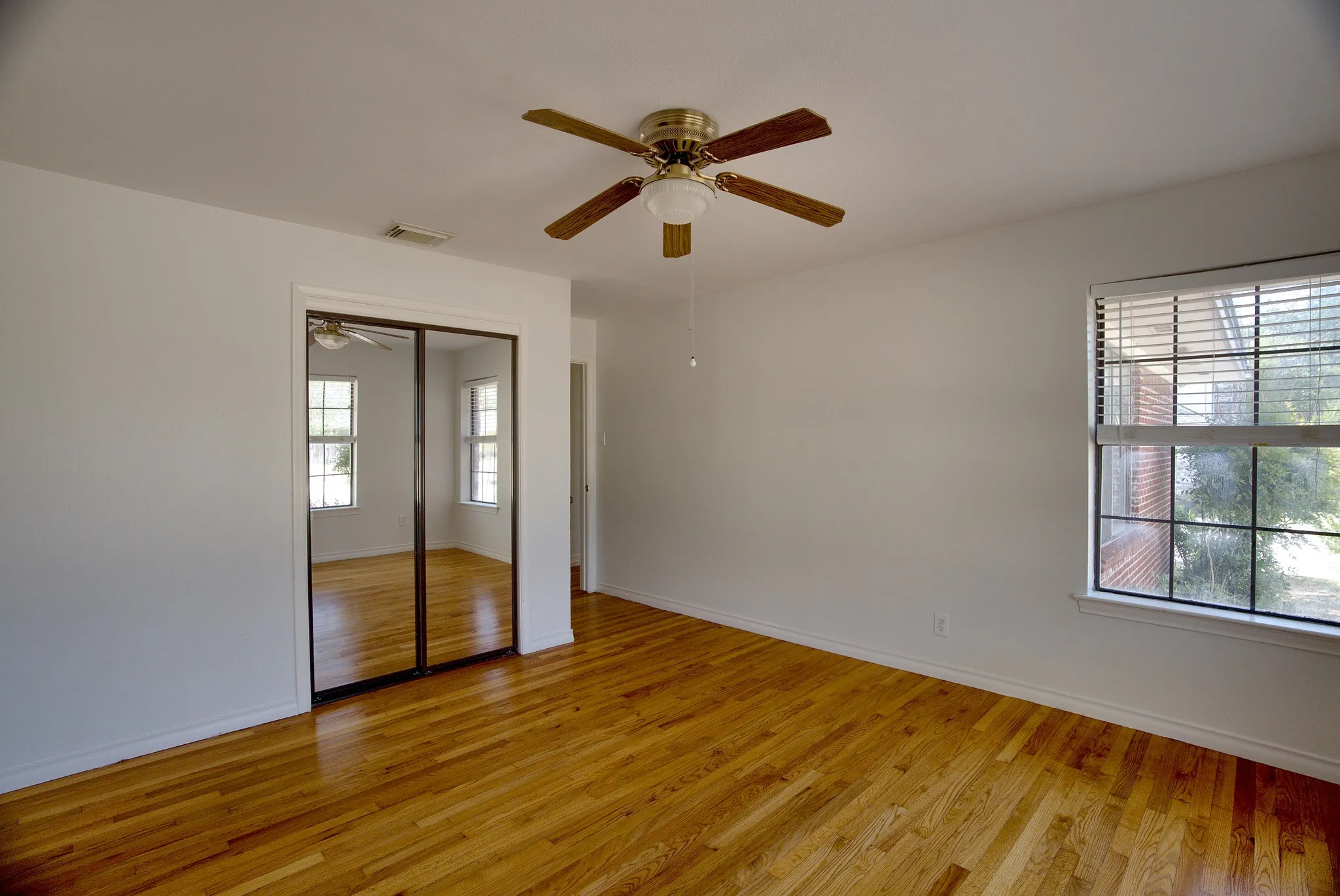 Wood-finish flooring, ceiling fan with light fixture, mirrored closet doors, and window with blinds