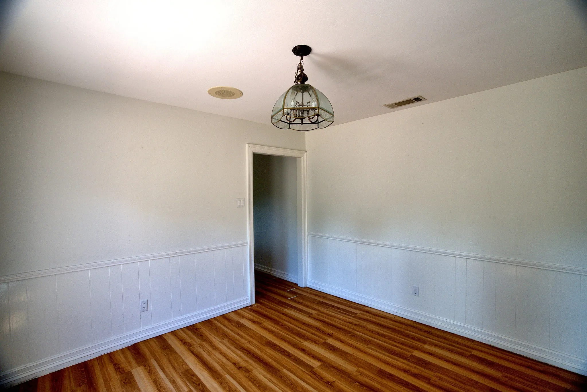 Wood-finish flooring, white paneled wainscoting, recessed ceiling speaker, and a decorative ceiling light fixture