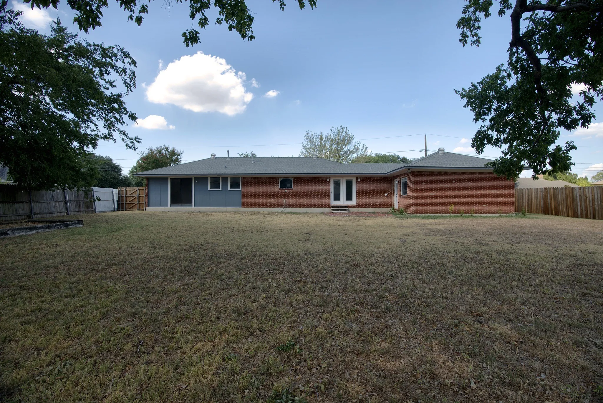 Expansive backyard featuring a brick and siding exterior, double-pane glass doors, and a partial privacy fence