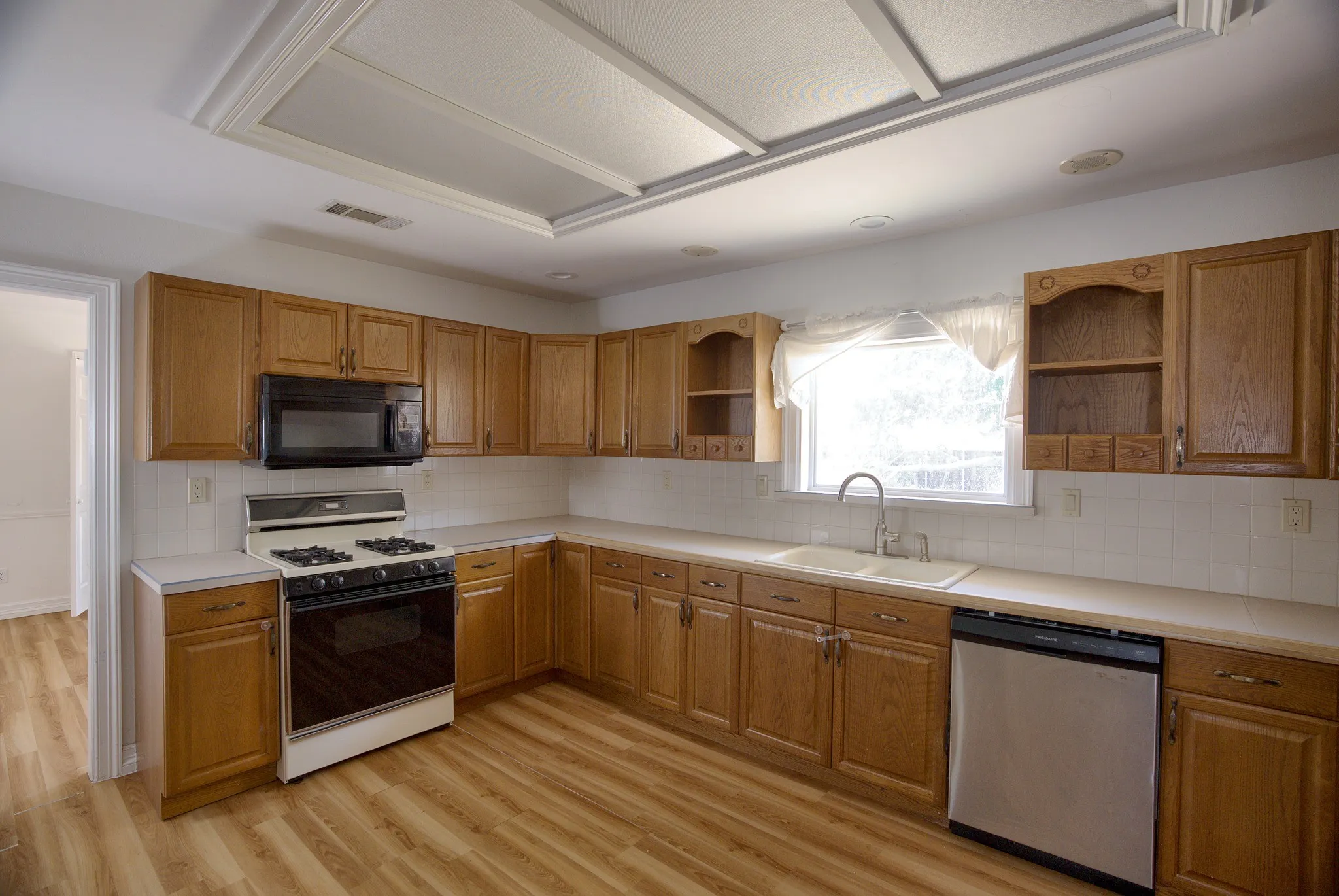 Laminate wood-finish flooring, recessed lighting, double basin sink, white tile backsplash, and light wood cabinetry